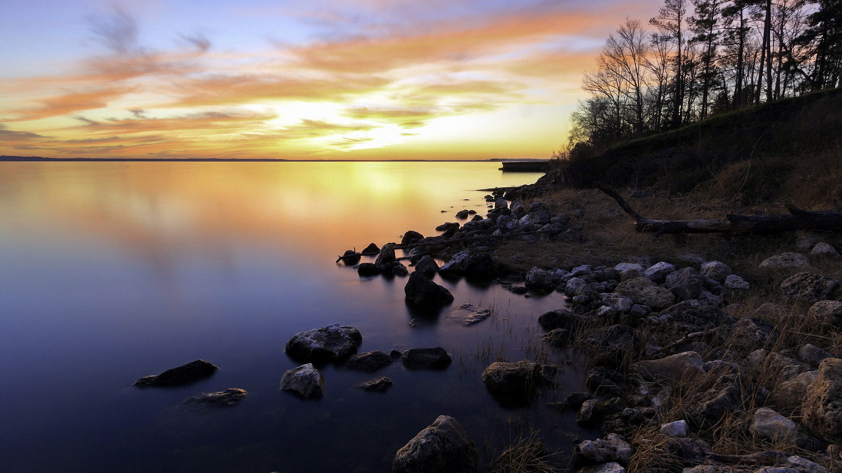 Sunset over a rocky lake shore with trees HD Wallpaper