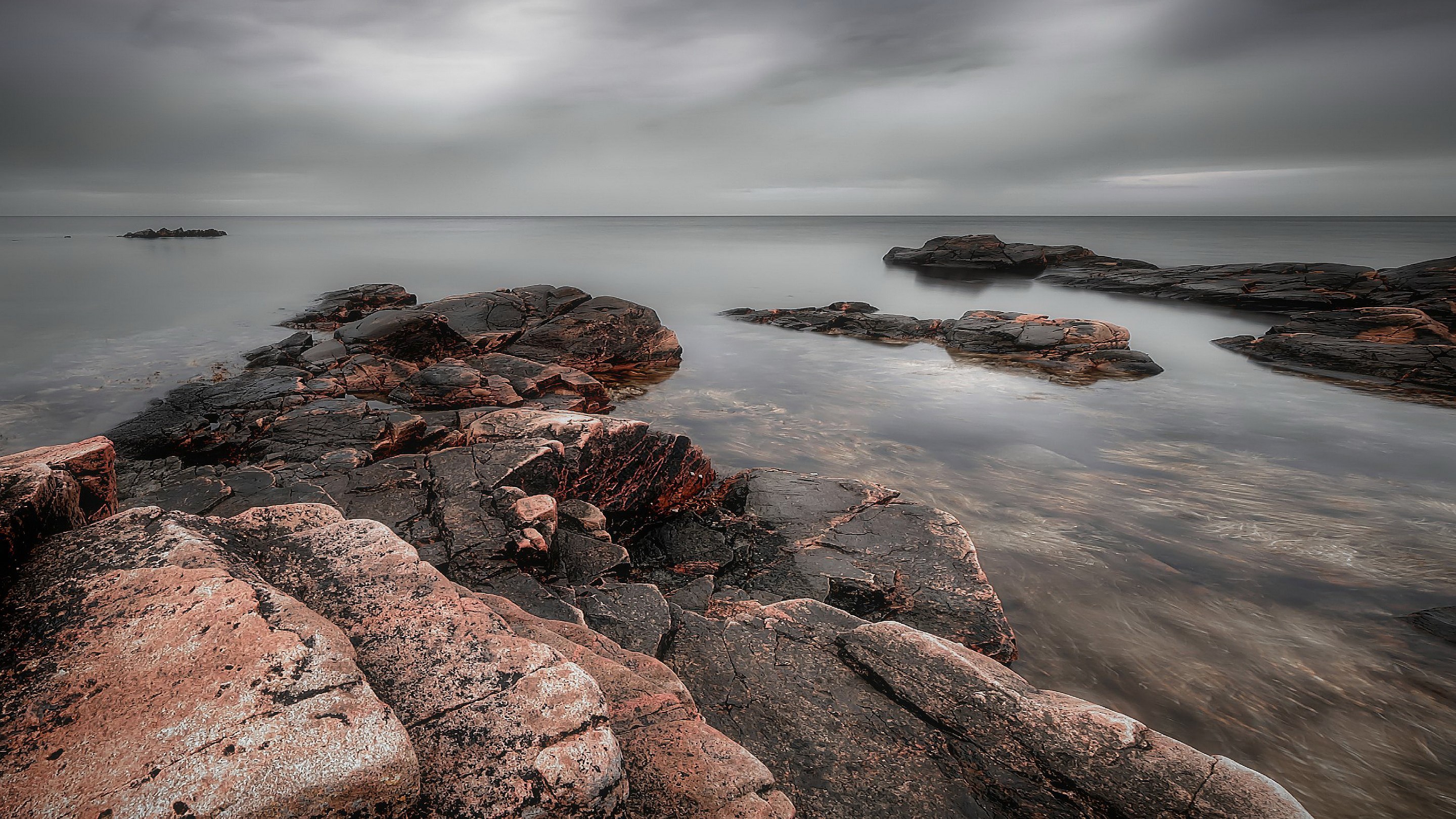 Rocky coastline with calm water under cloudy sky HD Wallpaper