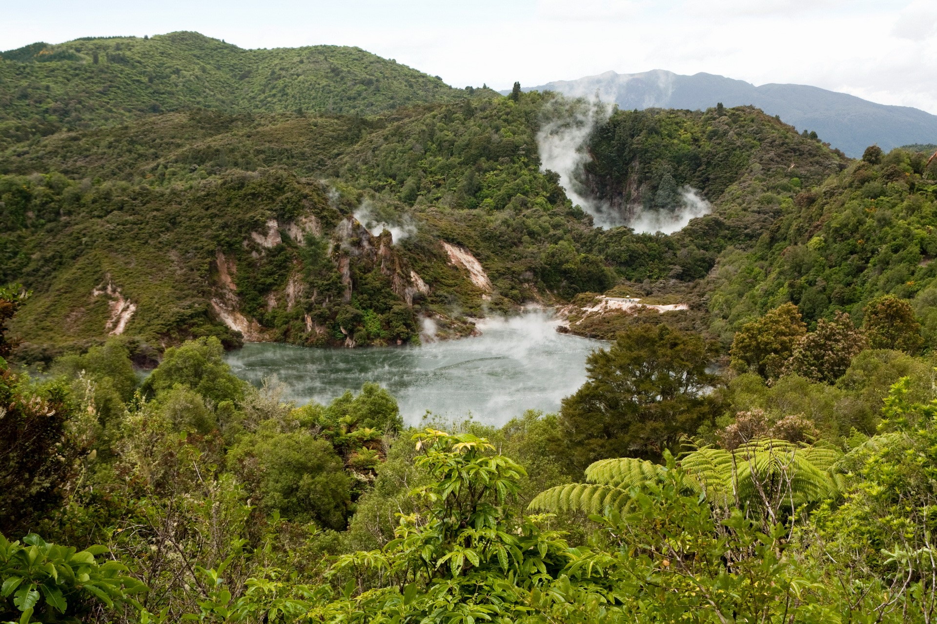 Geothermal lake surrounded by lush green mountains HD Wallpaper