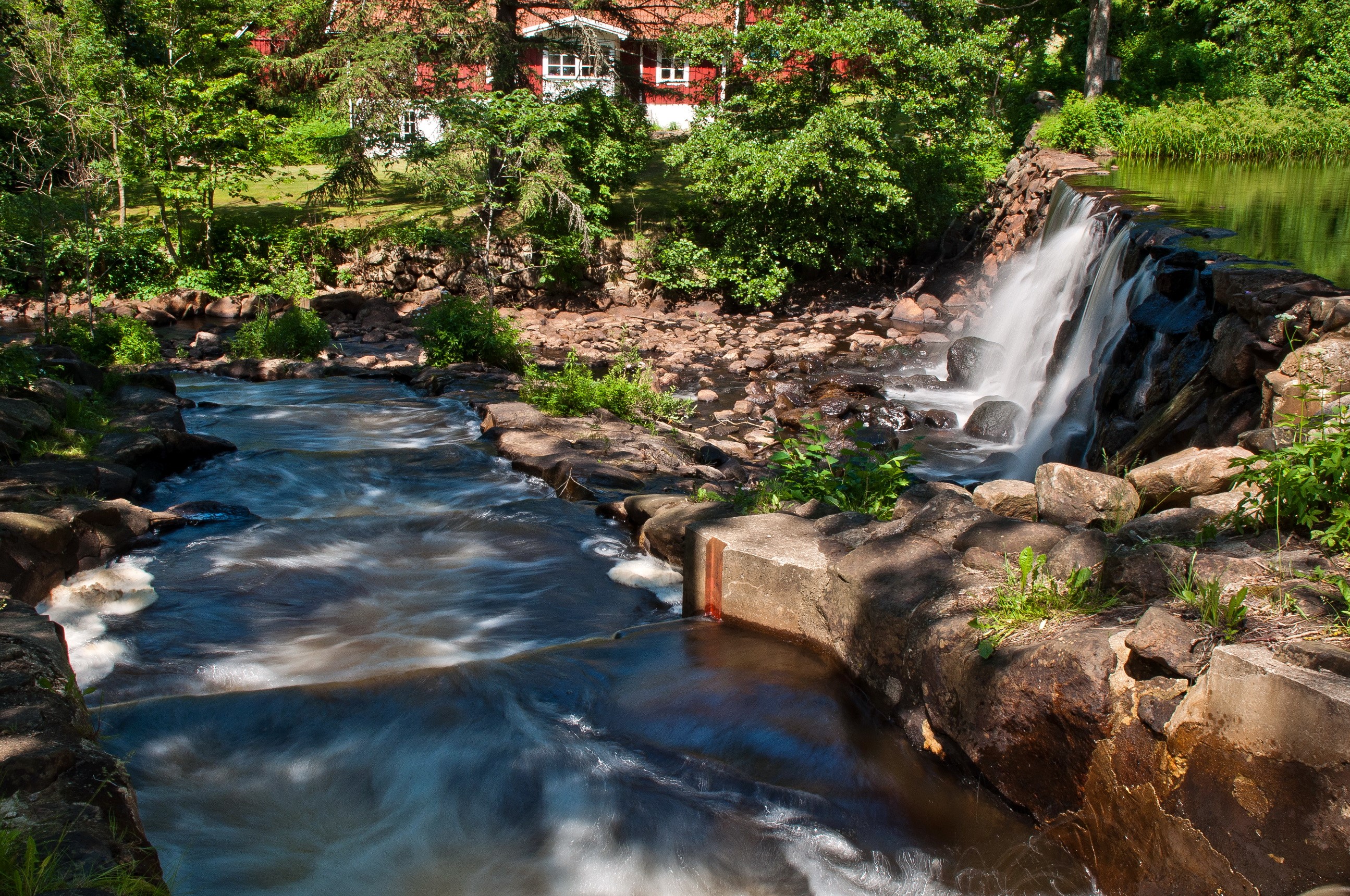 Waterfall flowing near a red house in a forest HD Wallpaper