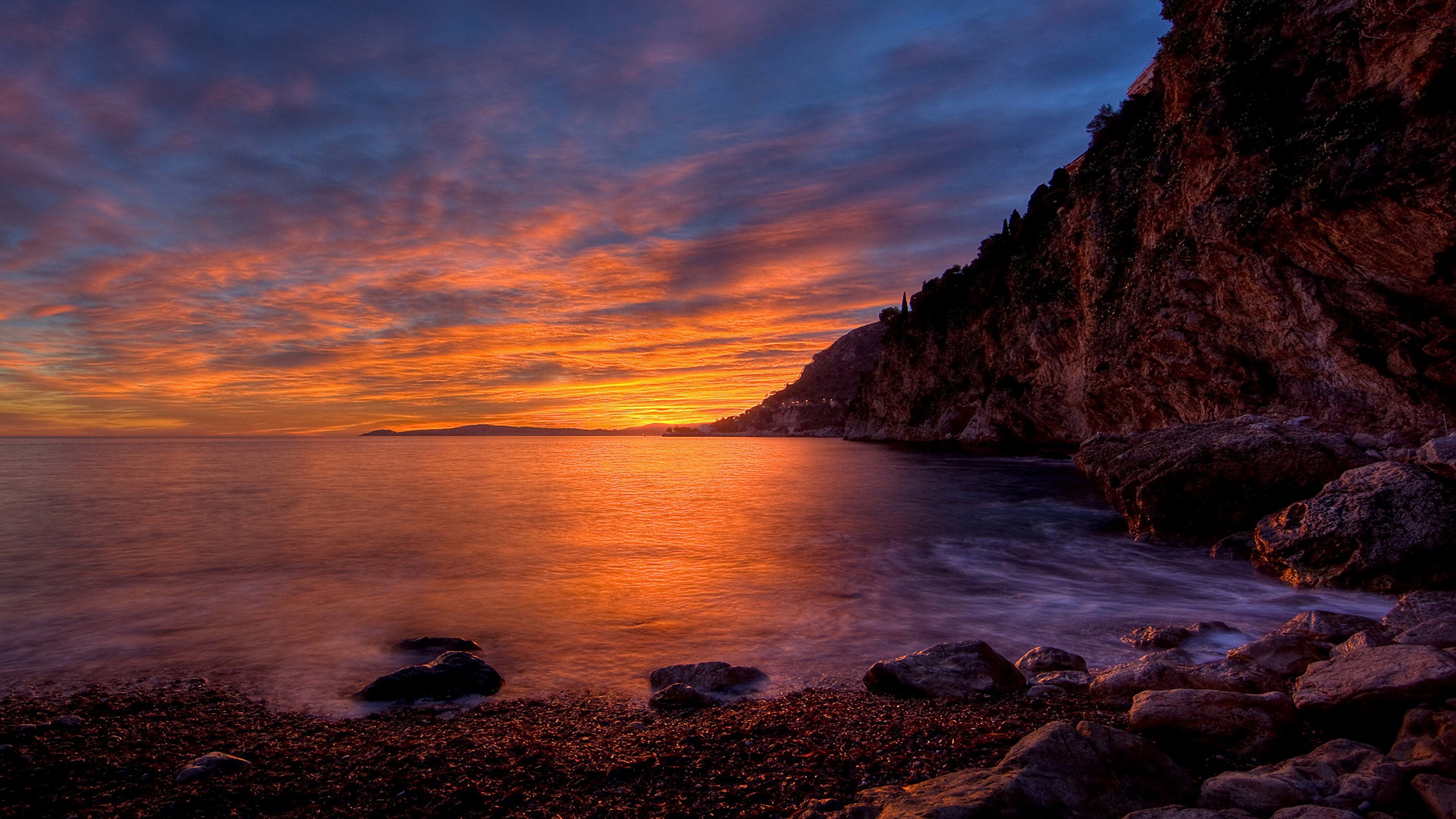 Sunset over a rocky coastline with dramatic clouds HD Wallpaper