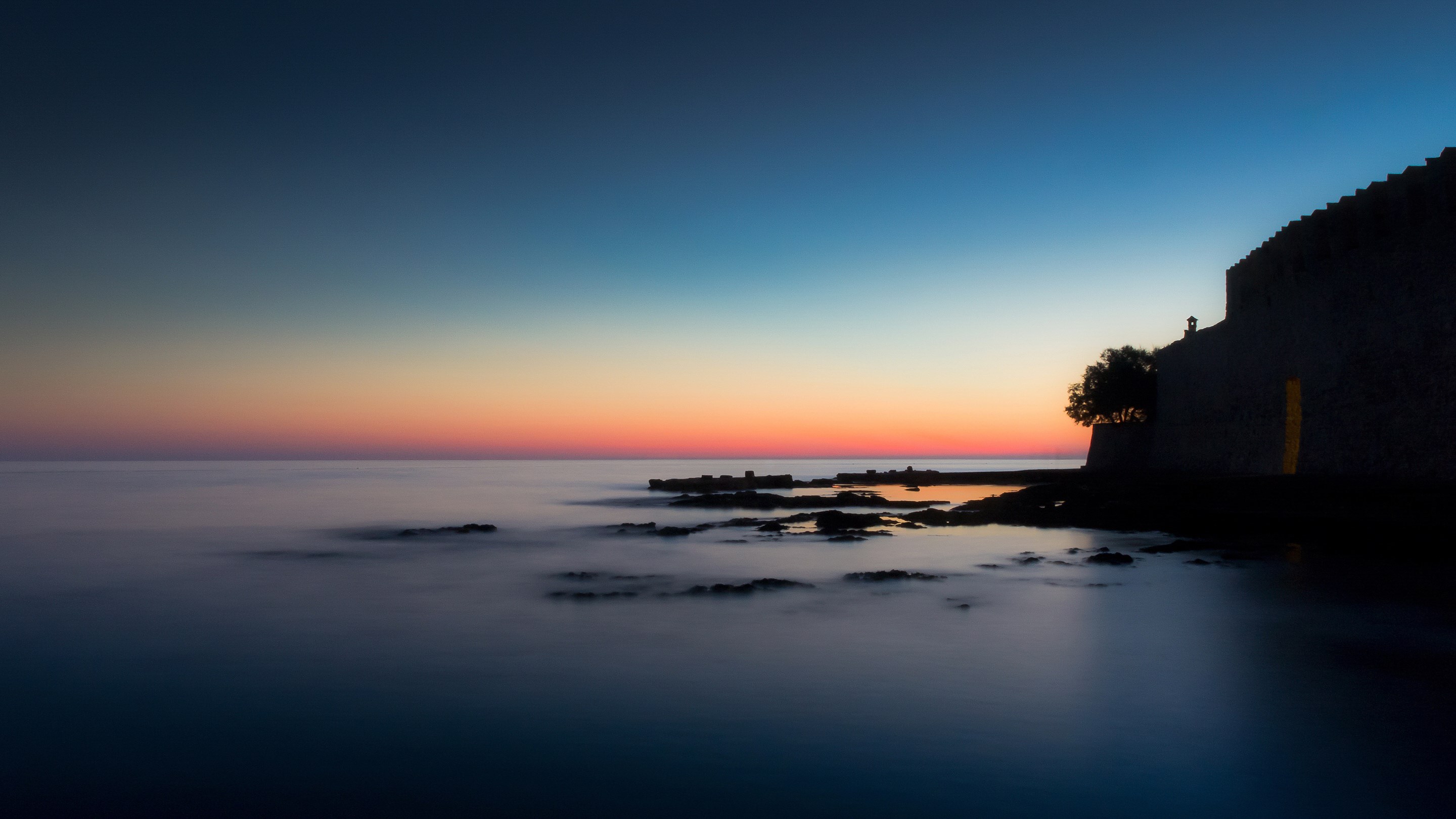Sunset over the sea with a stone wall and tree HD Wallpaper