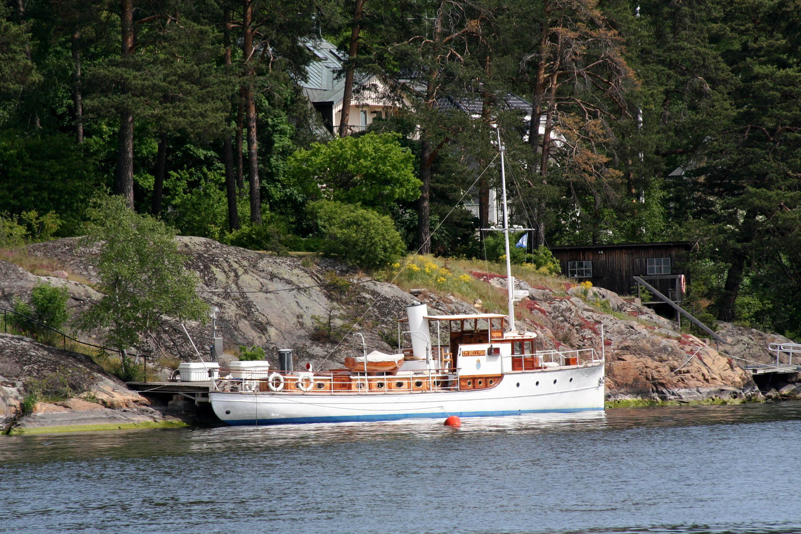 White and wooden boat docked by rocky shore with trees HD Wallpaper