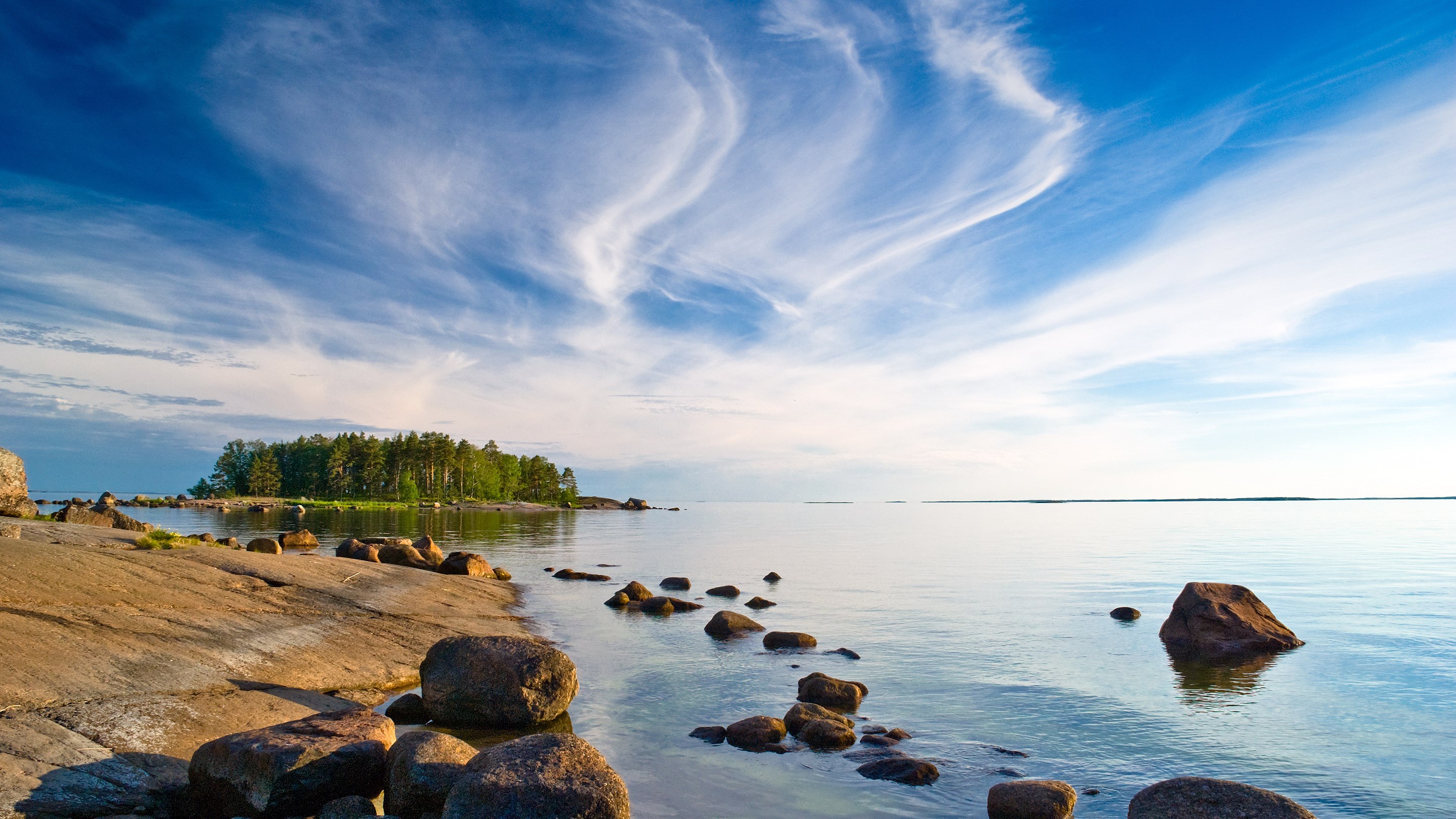 Rocky shoreline with trees and a calm sea under a cloudy sky HD Wallpaper