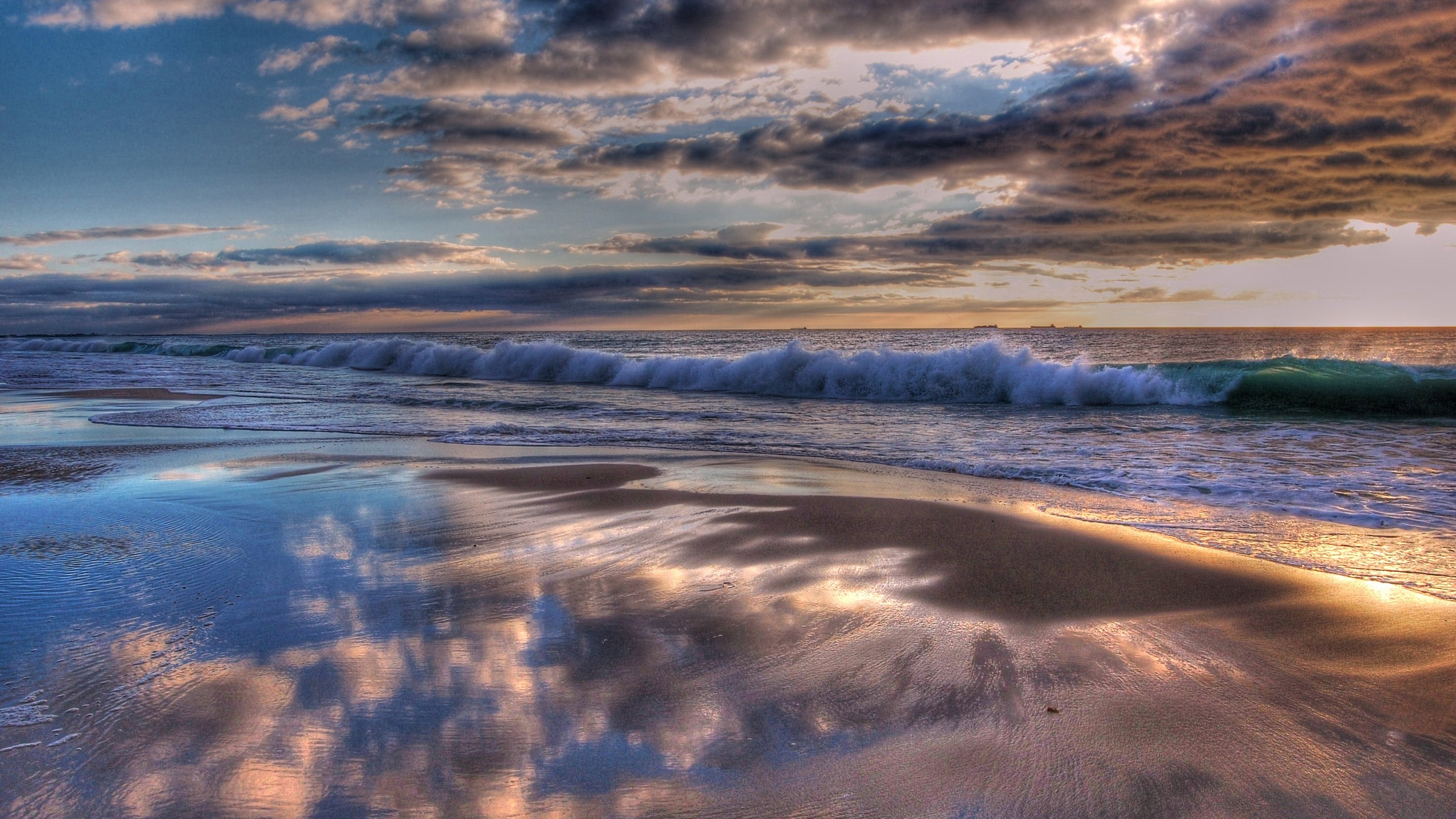 Ocean waves crashing on a sandy beach at sunset HD Wallpaper
