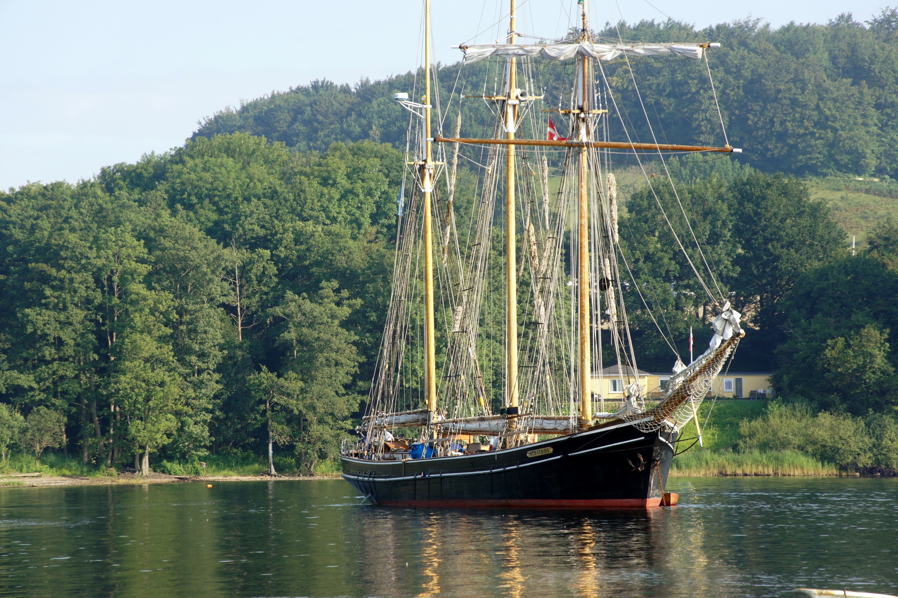 Tall ship sailing on water with green trees in background HD Wallpaper
