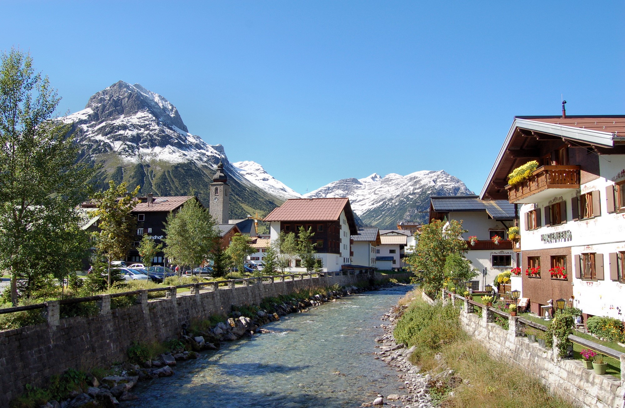 Alpine village with river and snow-capped mountains HD Wallpaper