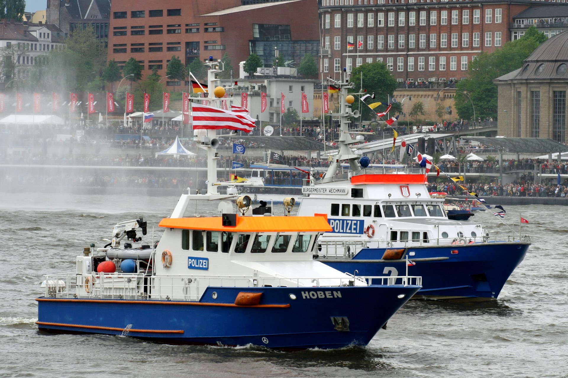 Two police boats on a river with spectators in the background HD Wallpaper