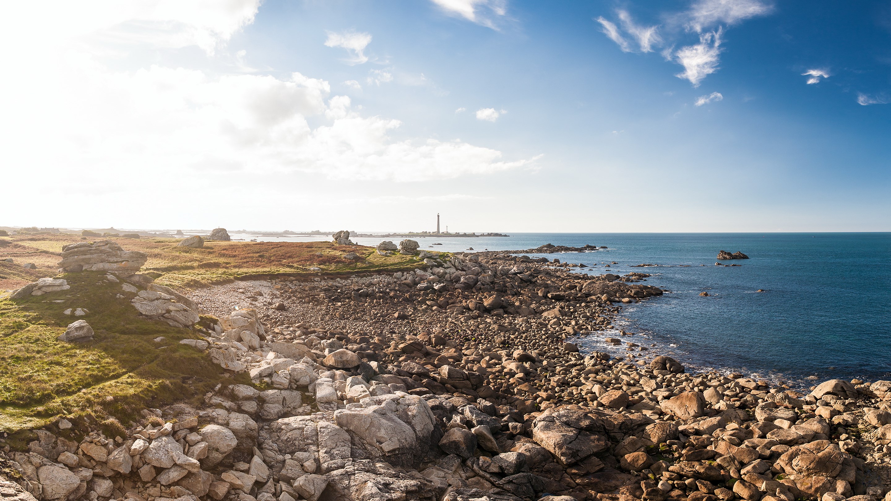 Rocky coastline with a lighthouse in the distance HD Wallpaper