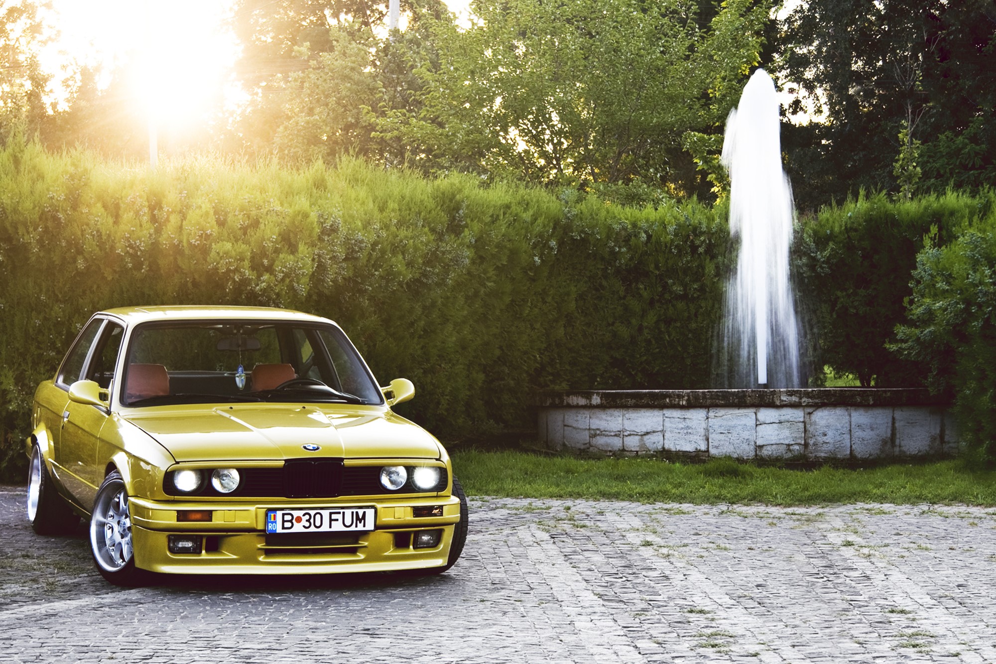Yellow BMW E30 parked near a fountain HD Wallpaper