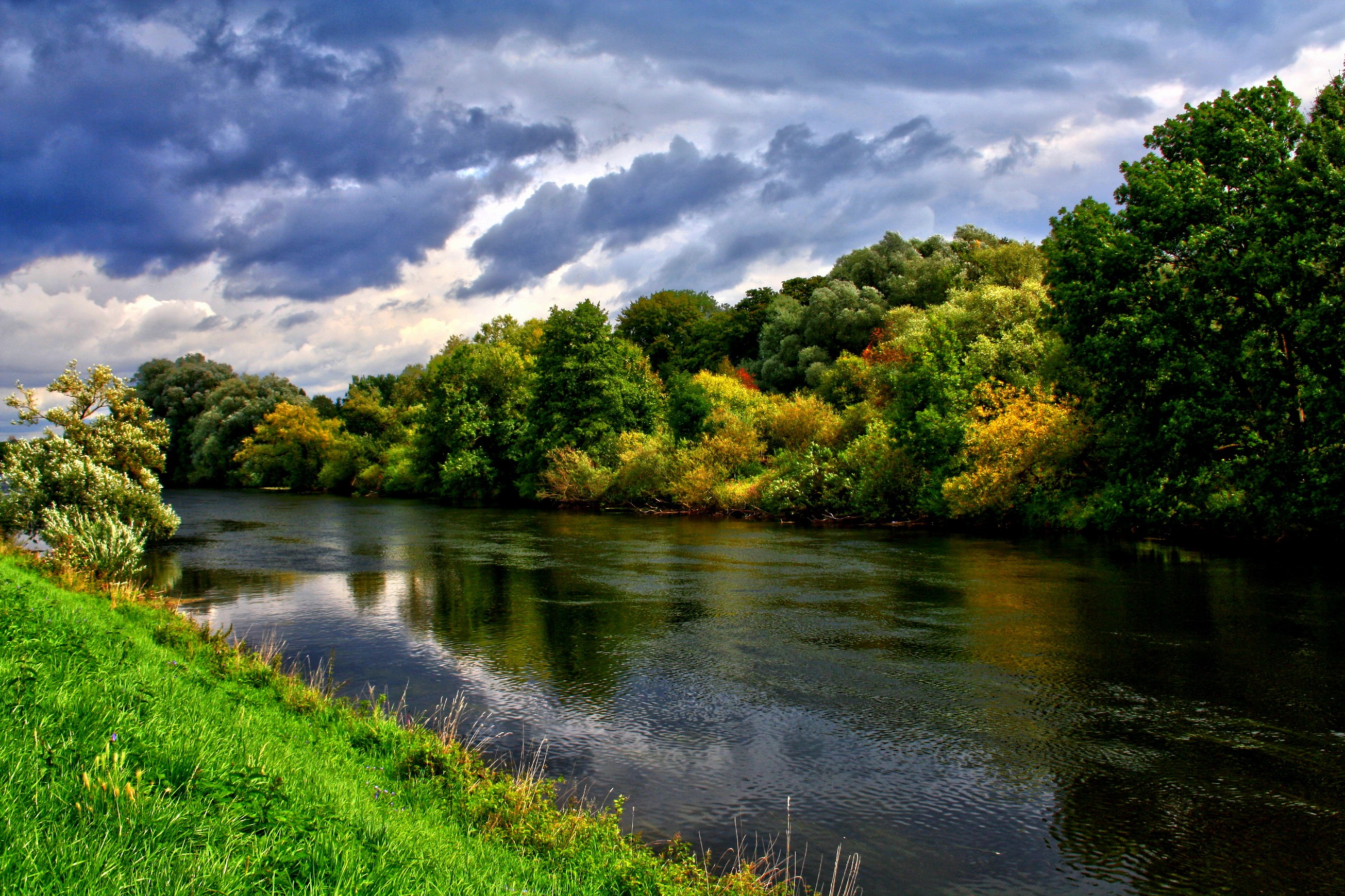 River flowing through a tree-lined landscape under a cloudy sky HD Wallpaper