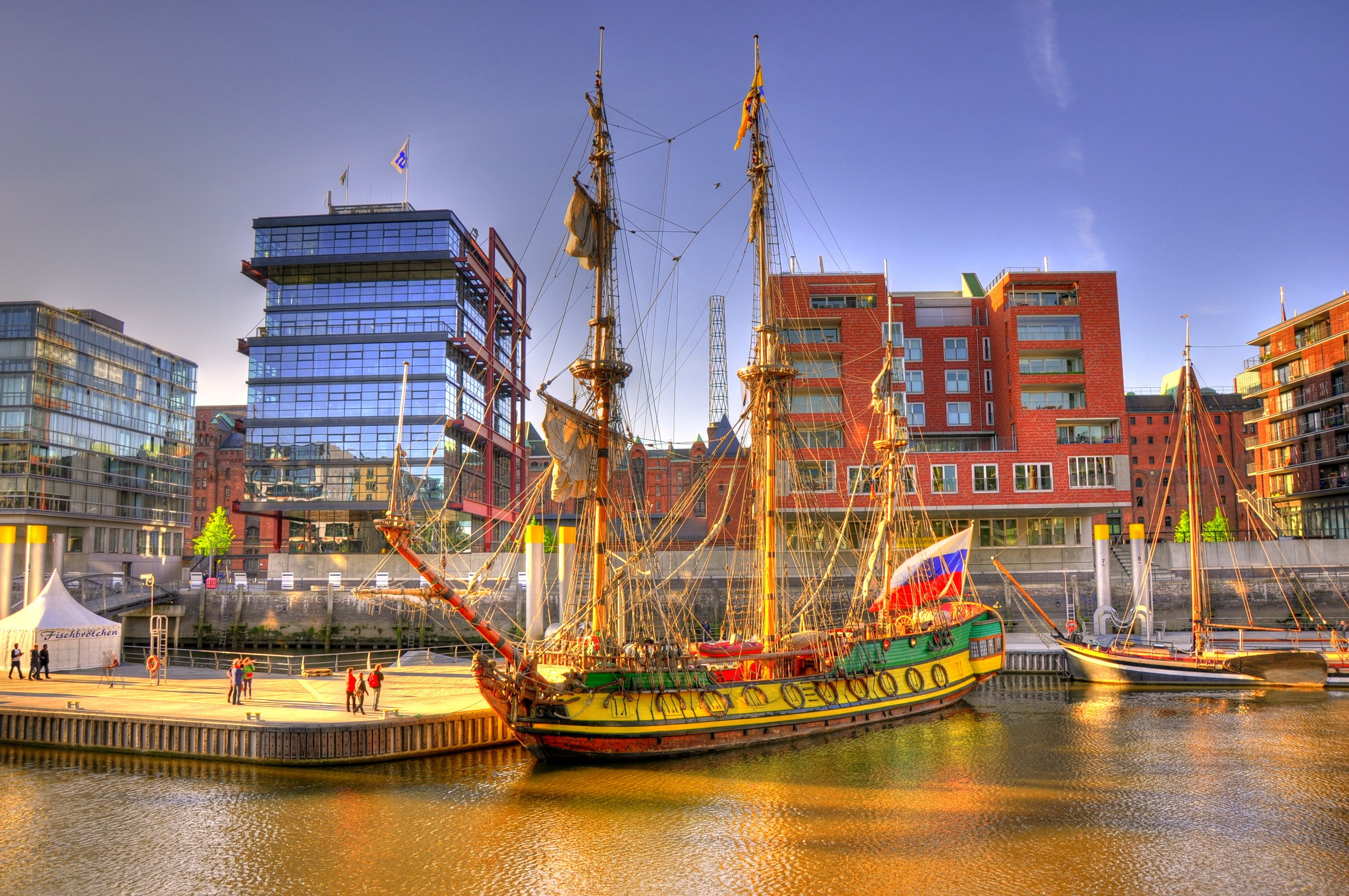 Tall ship docked in a modern harbor with brick buildings HD Wallpaper