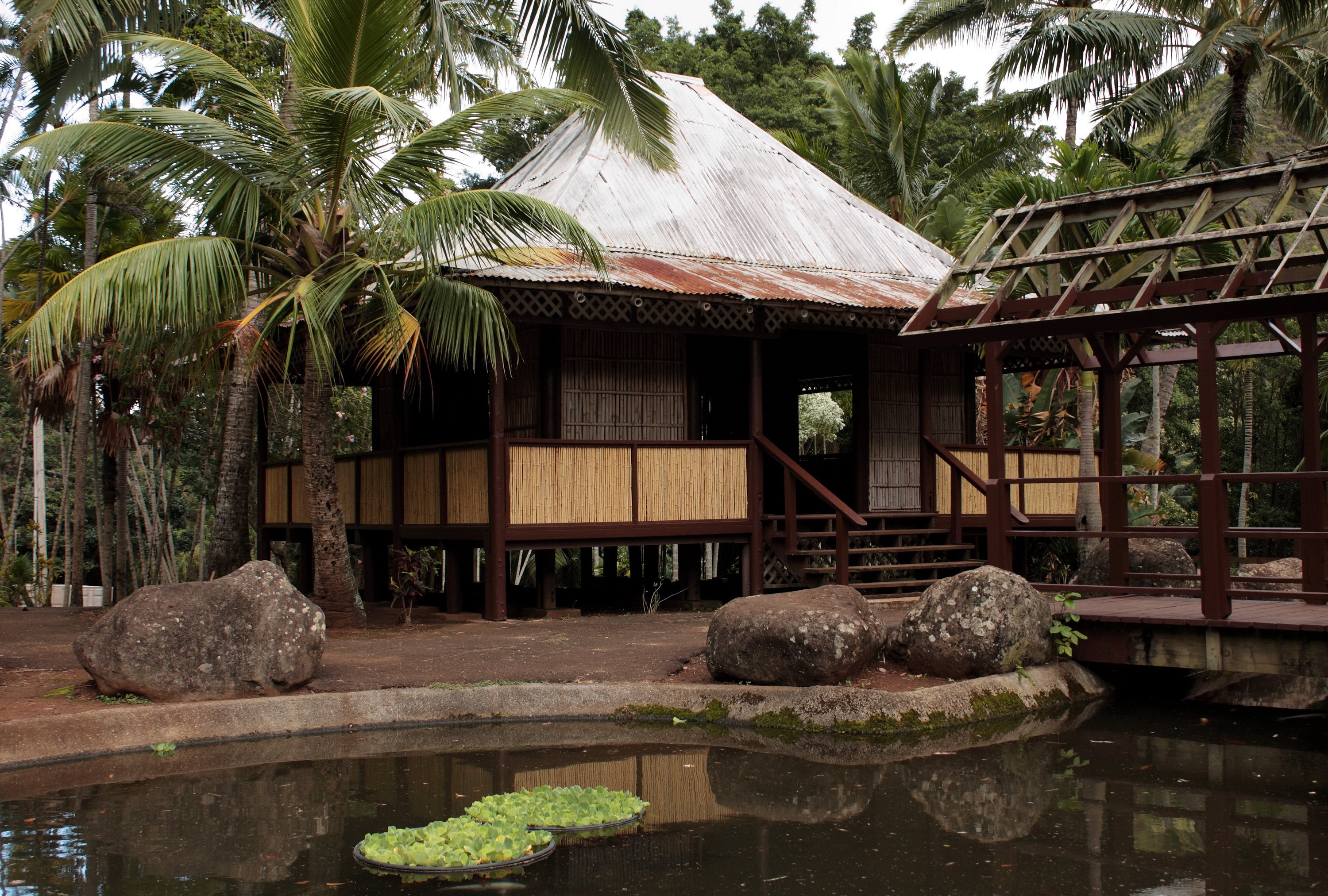 Traditional stilt house by a pond with palm trees HD Wallpaper