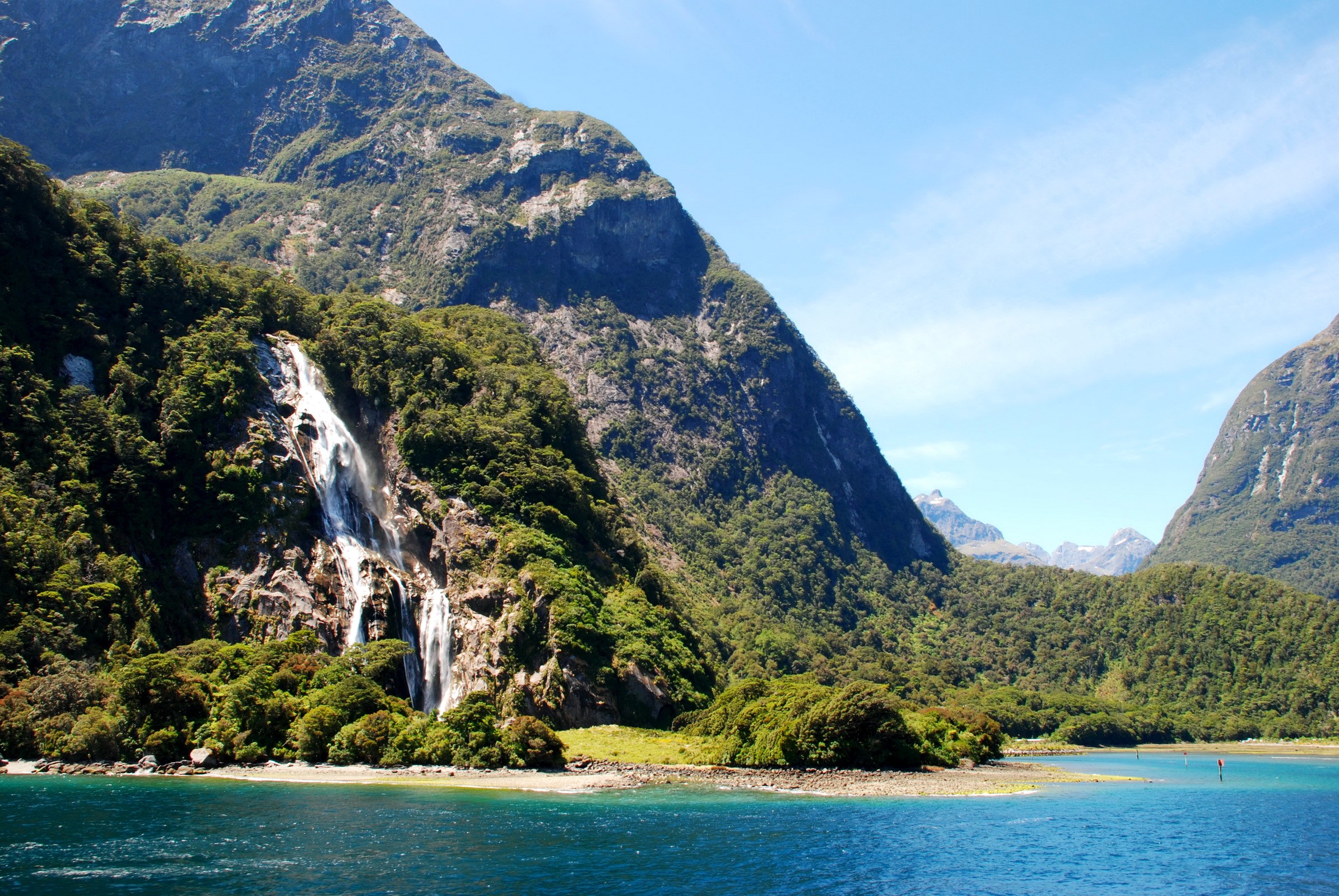 Waterfall cascading down a mountain into a blue lake HD Wallpaper