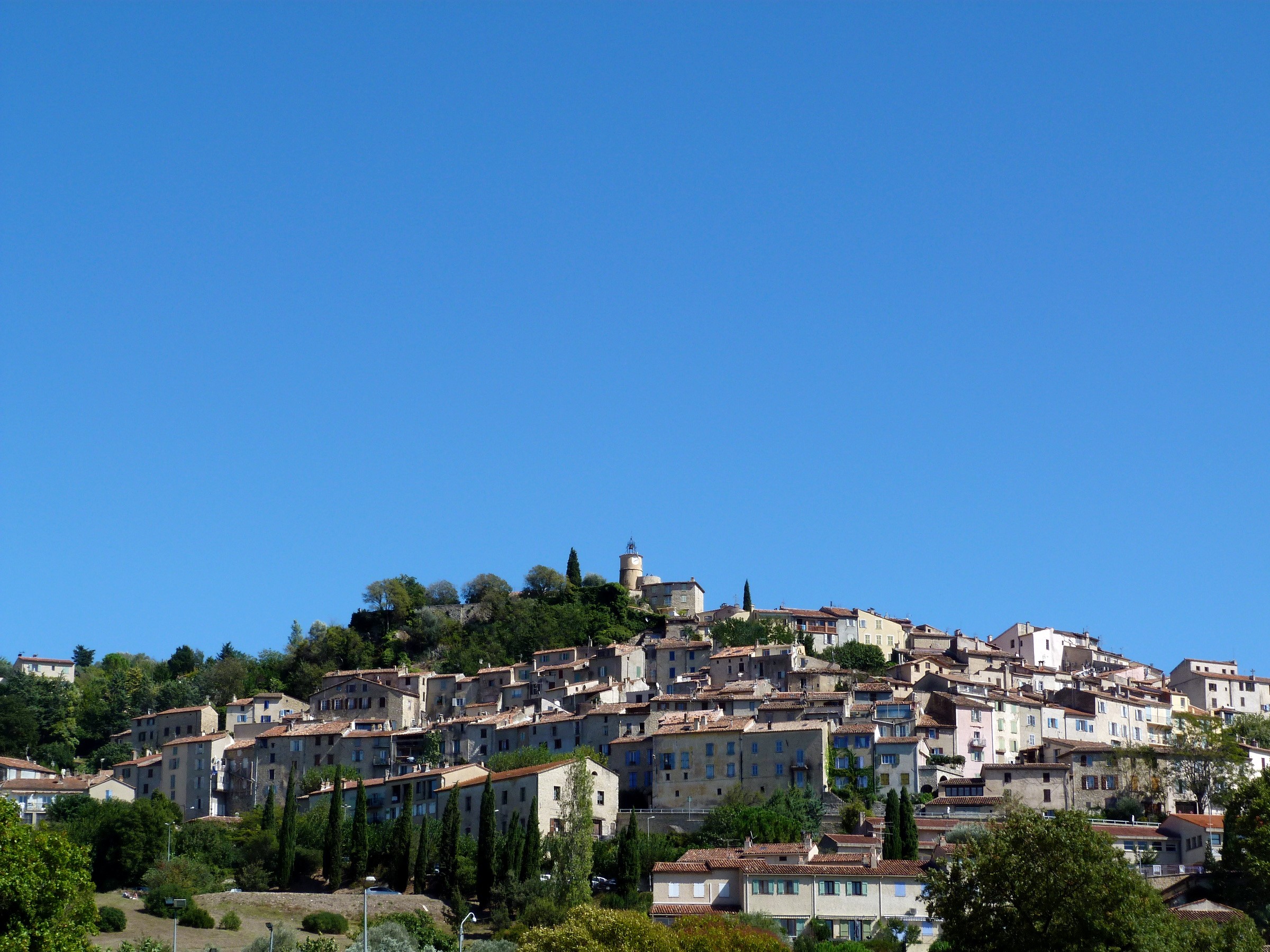 Hillside village with buildings and trees under blue sky HD Wallpaper