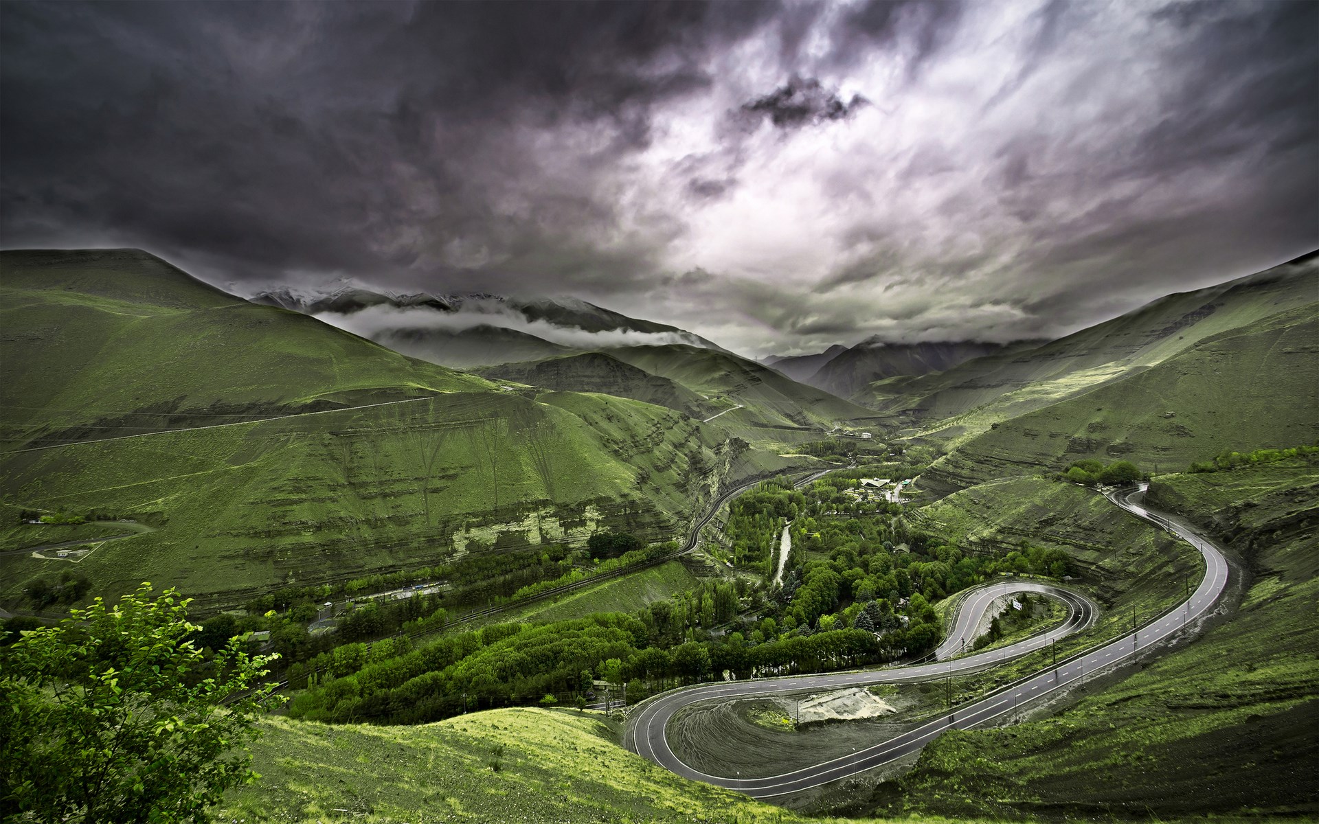 Winding mountain road through green valleys under stormy clouds HD Wallpaper