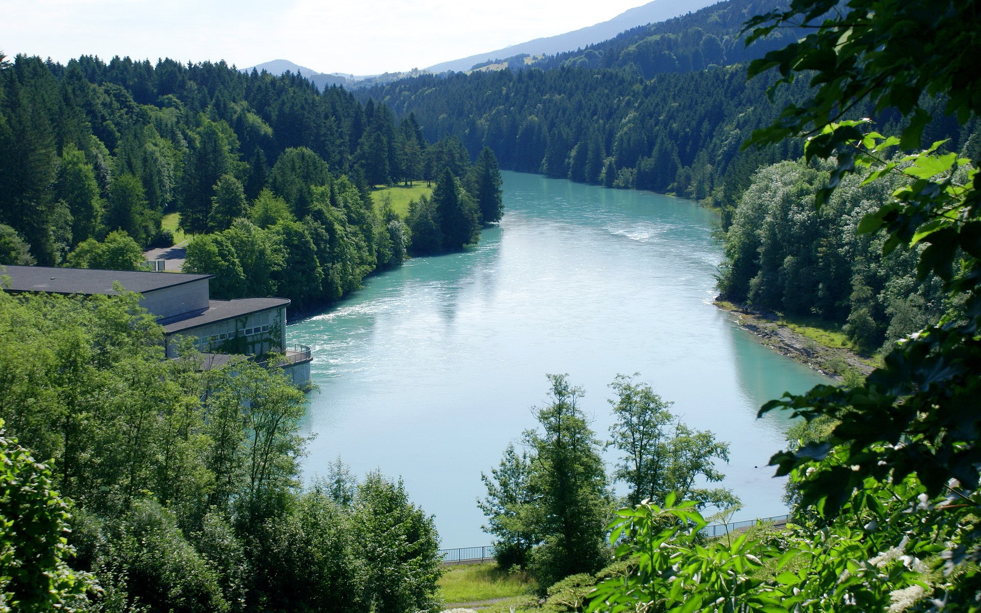 River flowing through a forested mountain landscape with a building HD Wallpaper