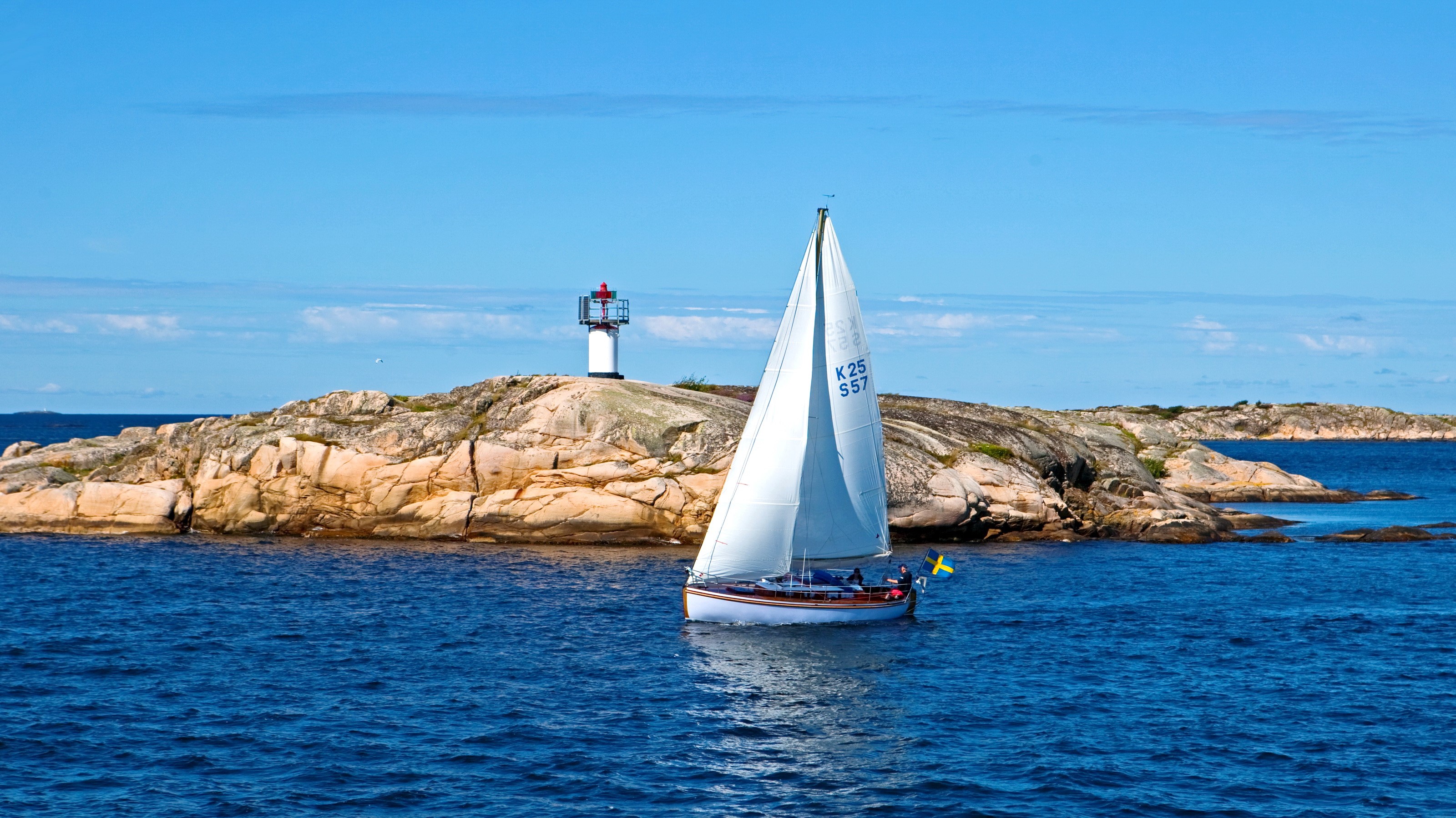 Sailboat near a lighthouse on a rocky island HD Wallpaper