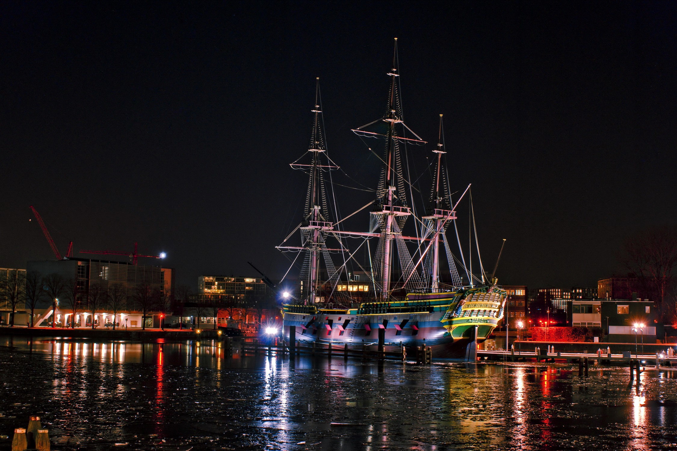 Tall ship docked at night with city lights and reflections HD Wallpaper