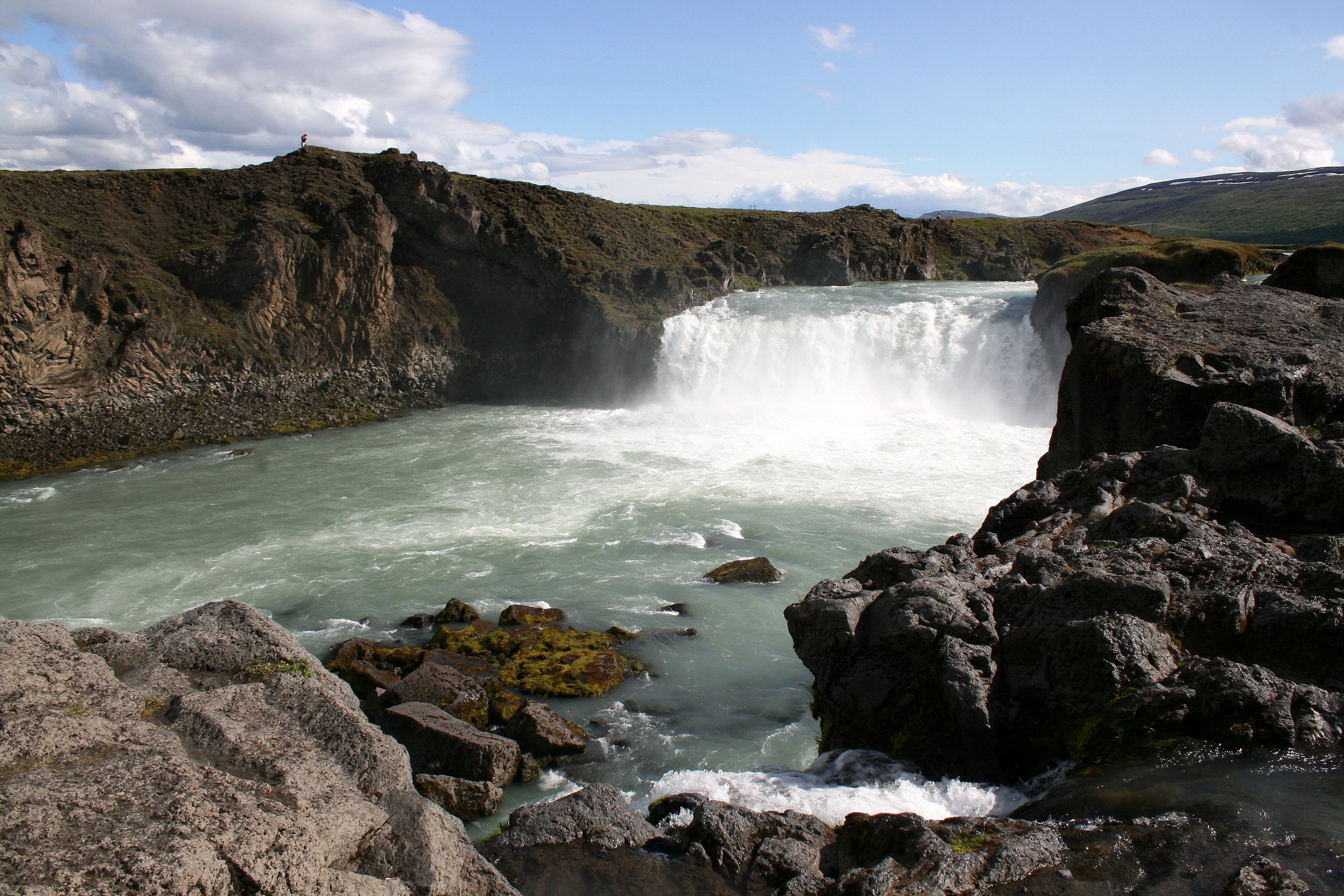 Waterfall cascading into a turquoise river with rocky shores HD Wallpaper