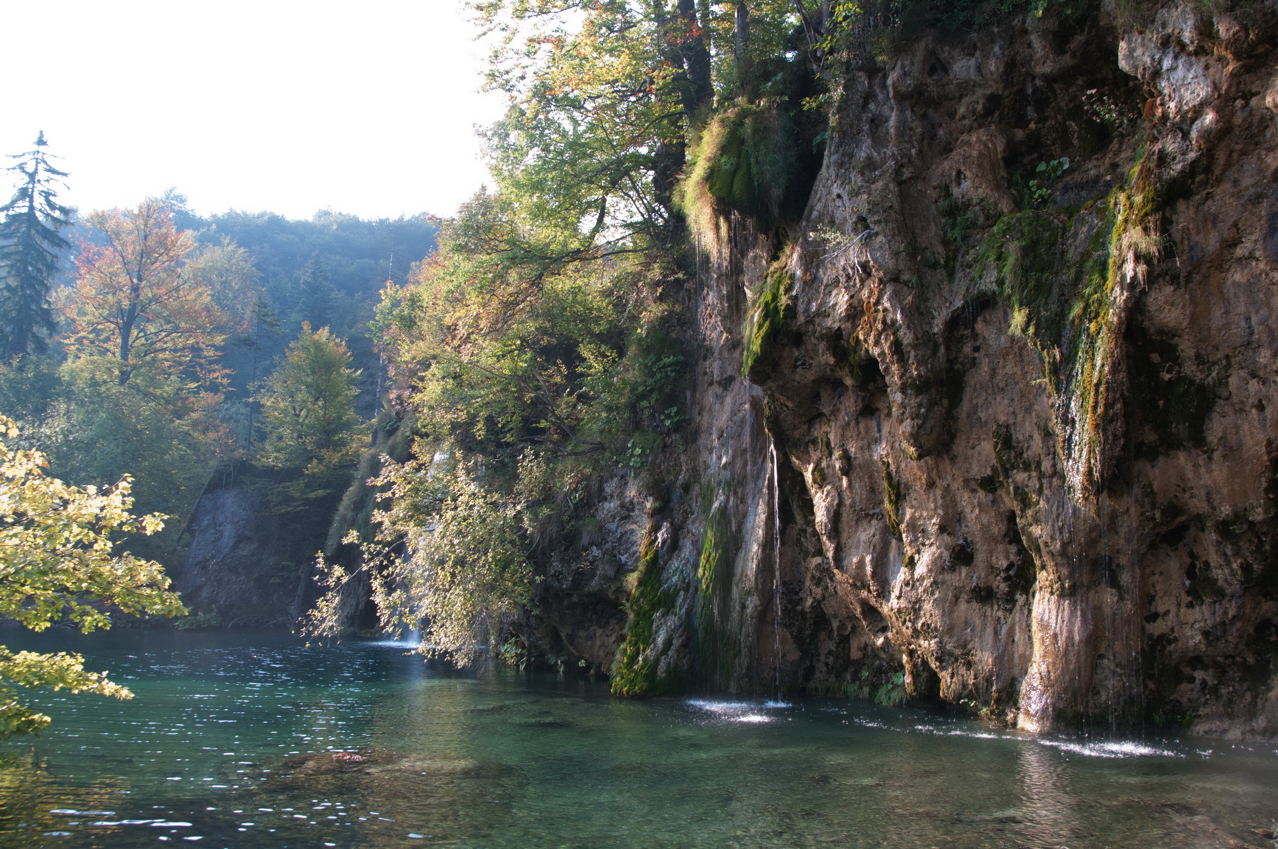 Waterfalls cascading over rocky cliffs into a clear lake HD Wallpaper