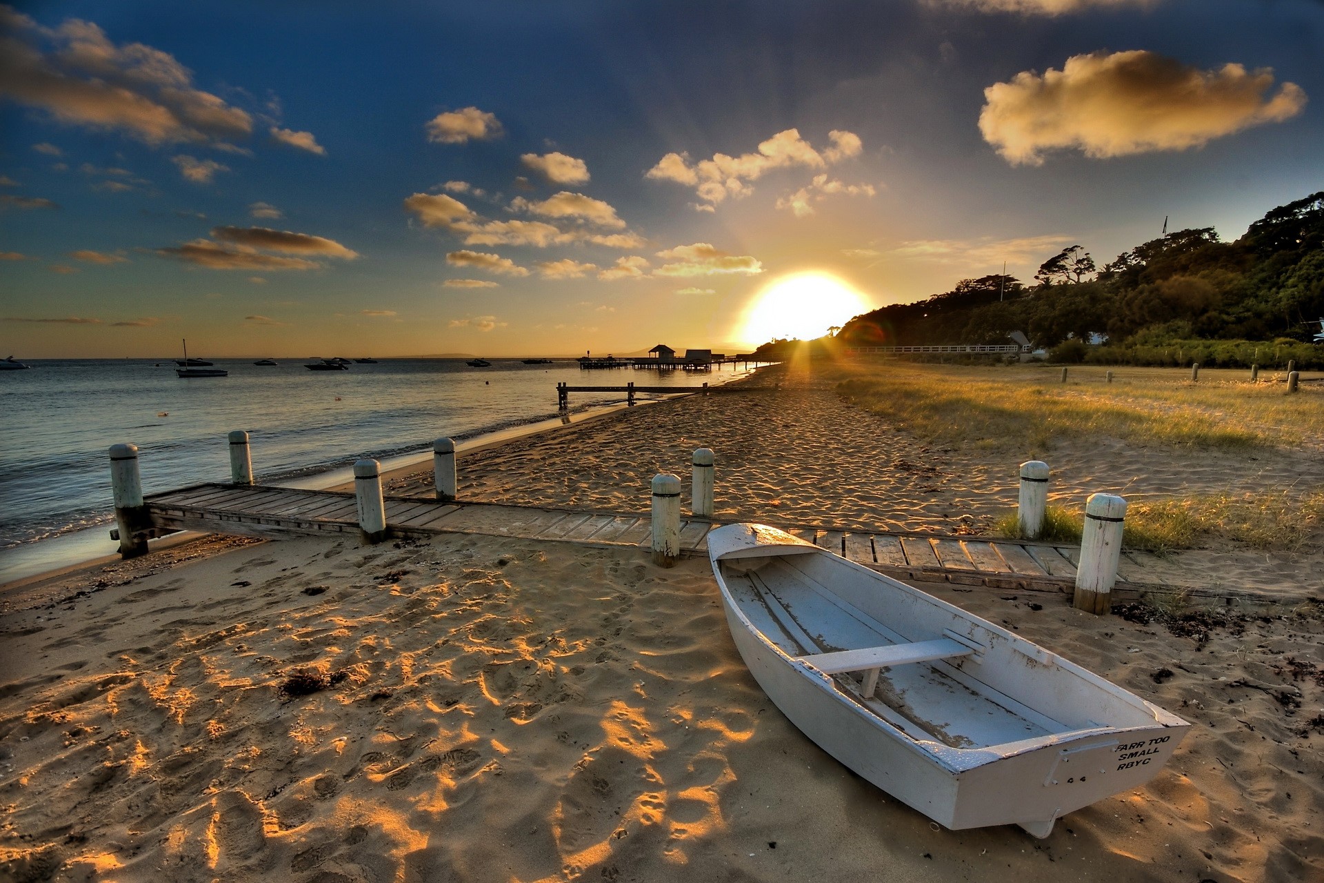 Sunset over a beach with a small boat and pier HD Wallpaper