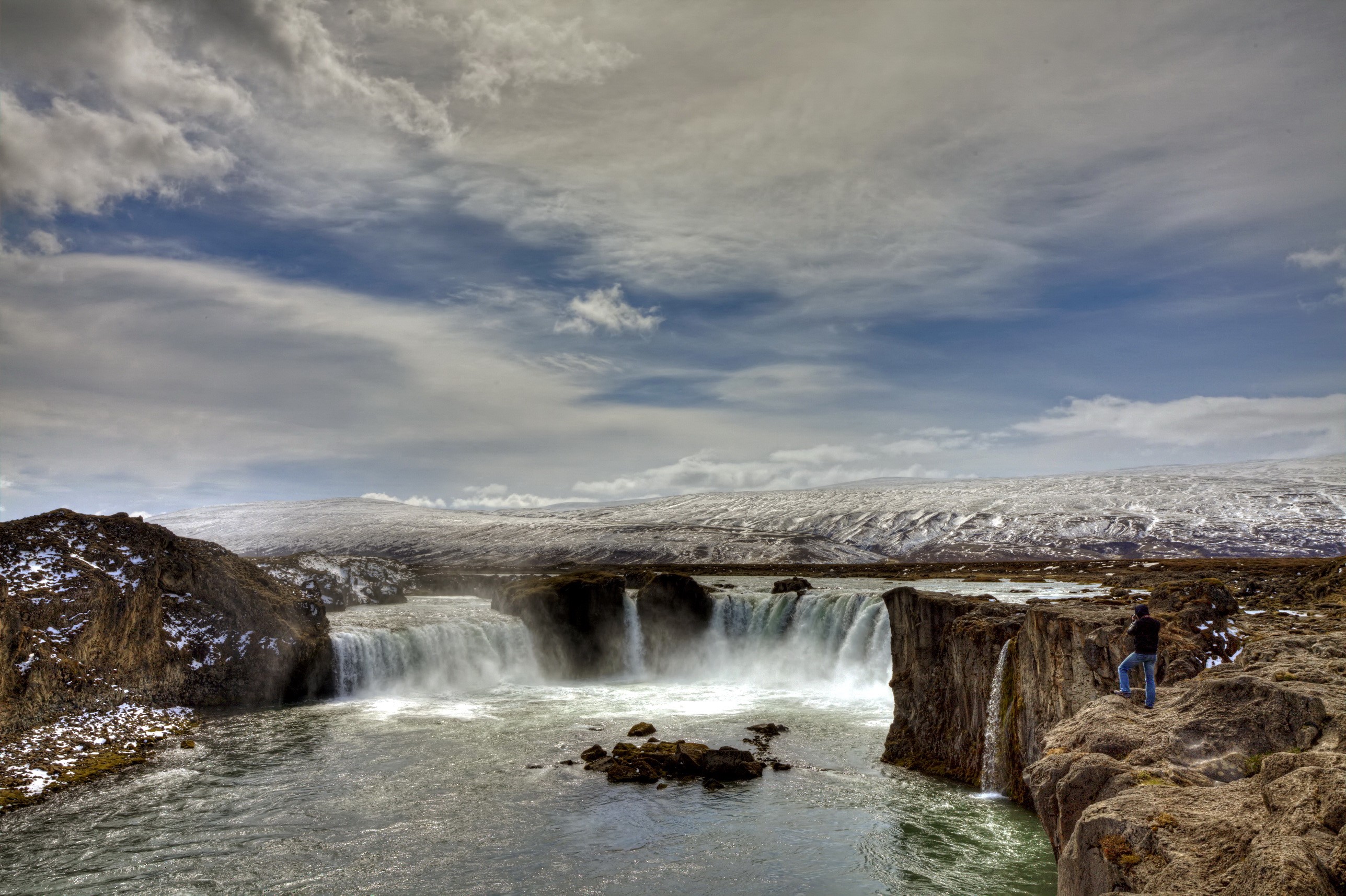 Man standing on cliff edge overlooking a waterfall HD Wallpaper