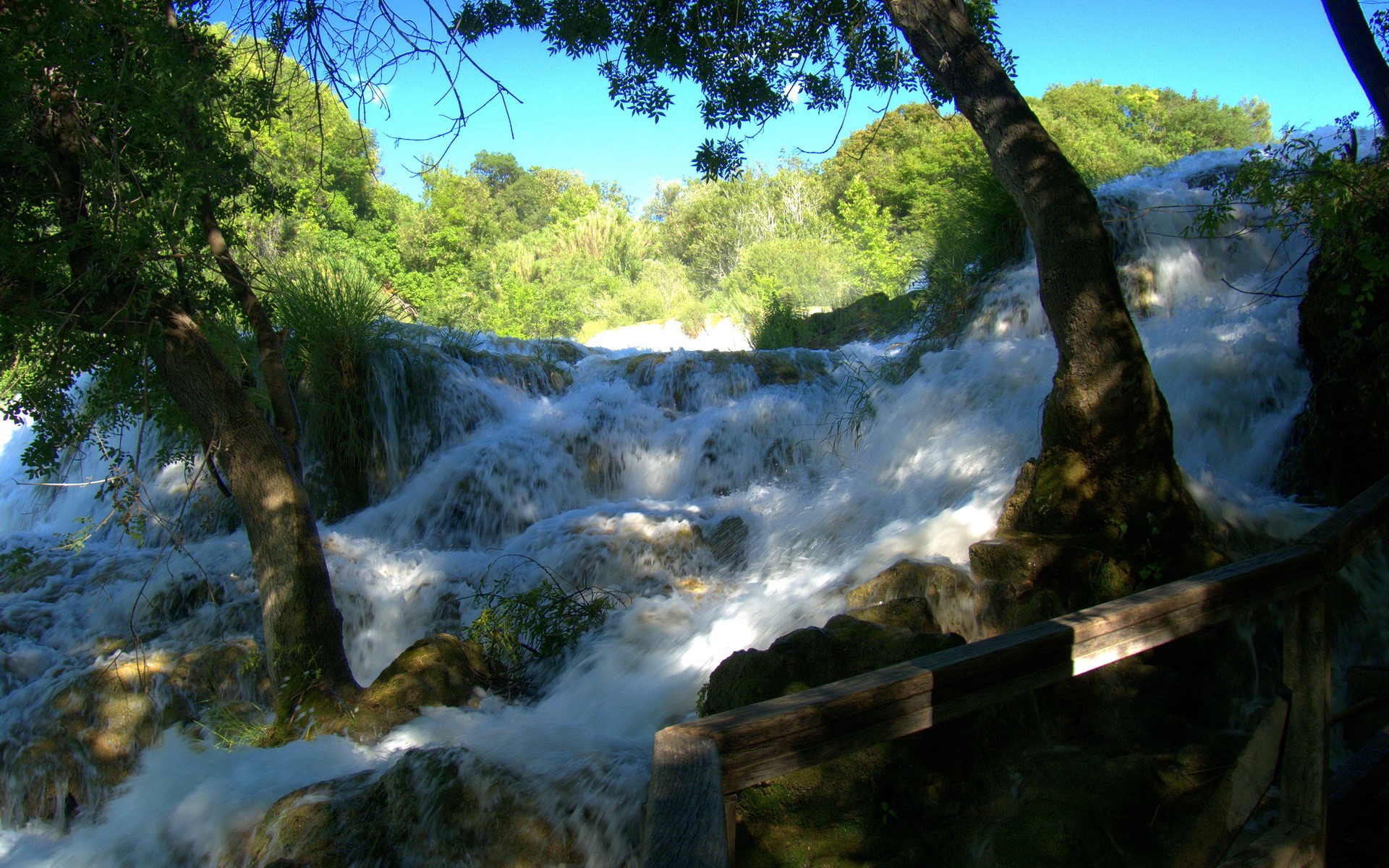 Waterfalls cascading over rocks with trees and blue sky HD Wallpaper