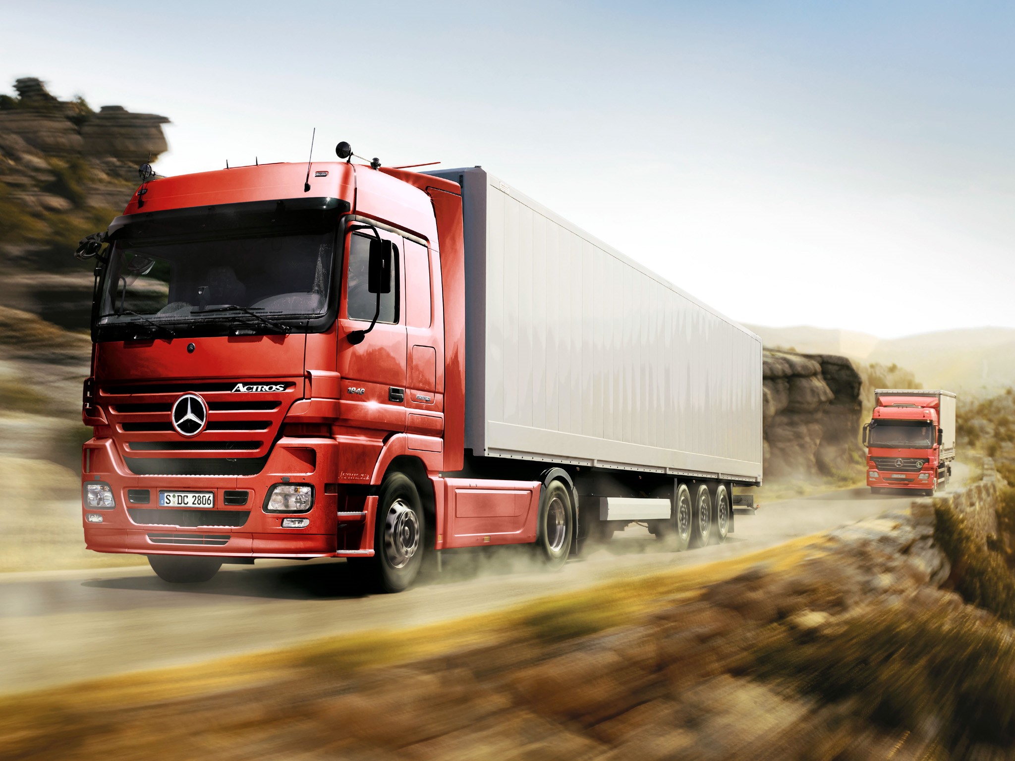 Two red Mercedes-Benz Actros trucks on a road HD Wallpaper