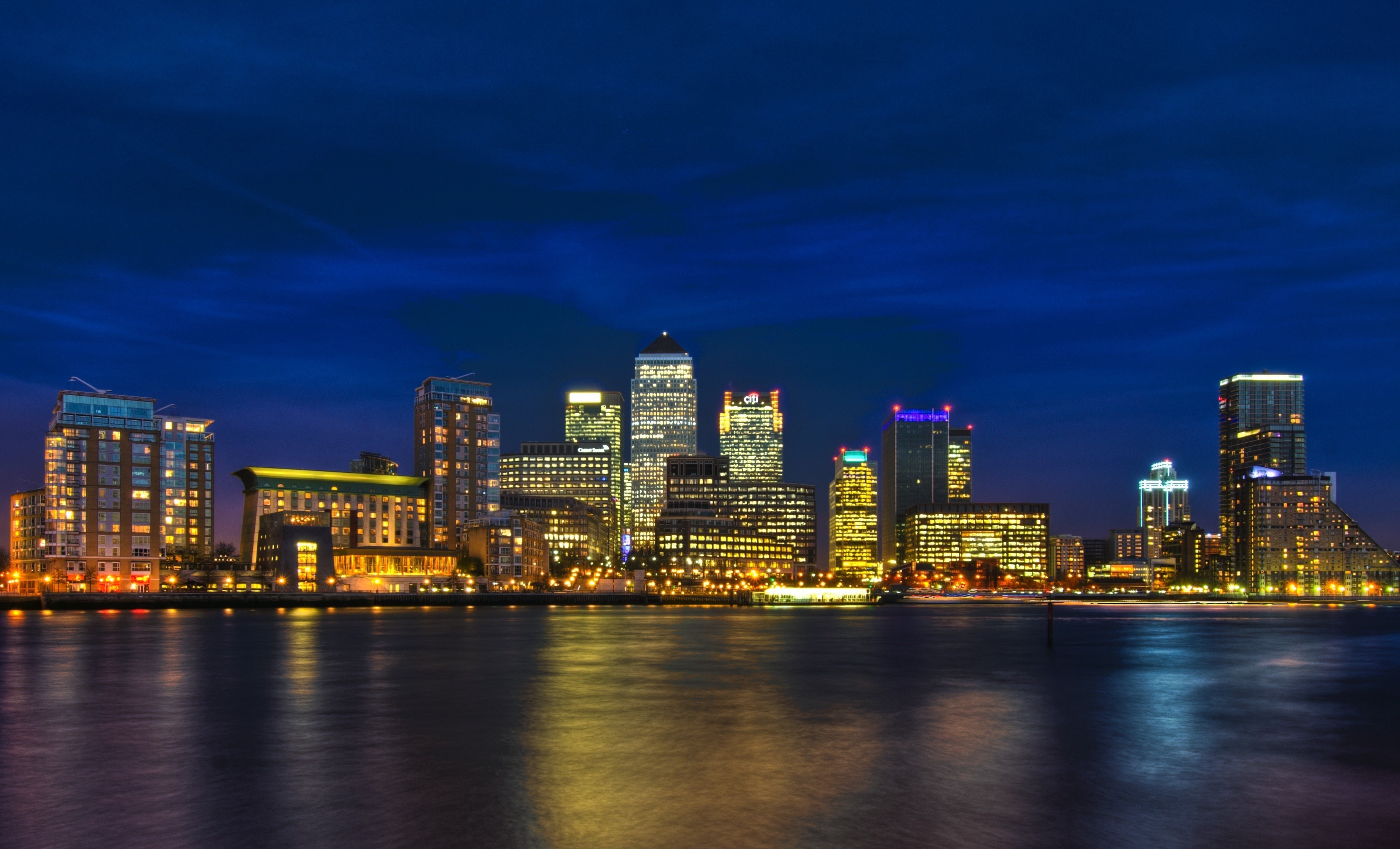 City skyline at night with reflections on water HD Wallpaper