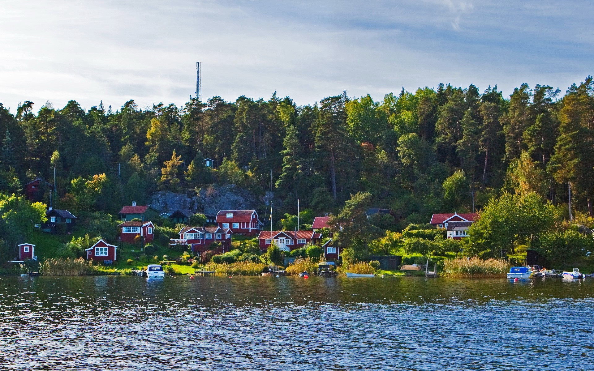 Red houses on a forested hillside by the water in Sweden HD Wallpaper