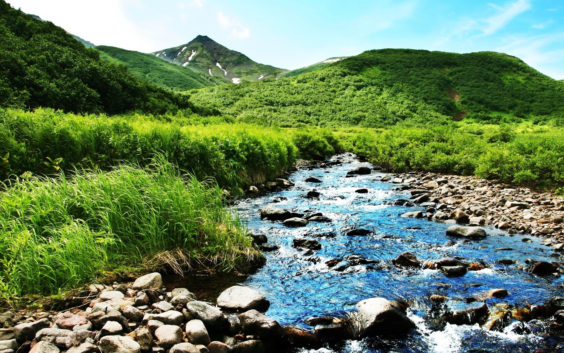 A clear blue river flows through a green mountain landscape HD Wallpaper