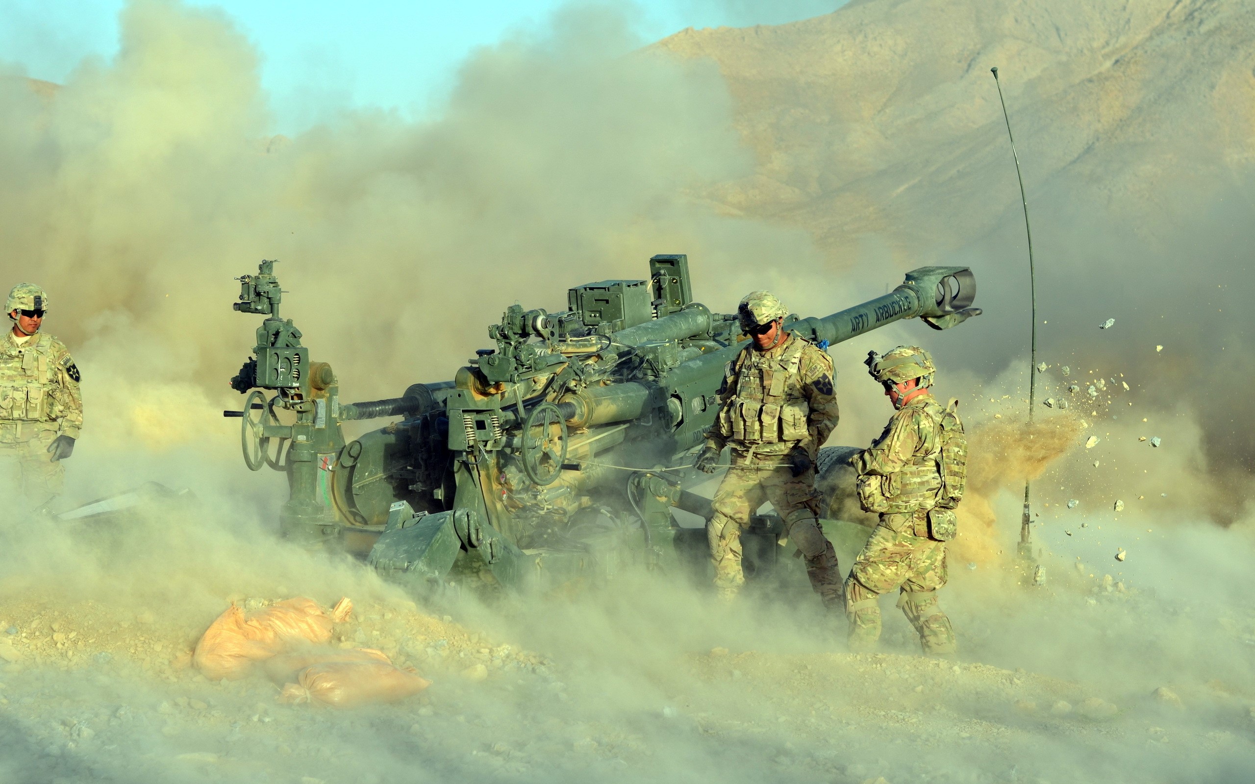 Soldiers firing a cannon in a desert HD Wallpaper