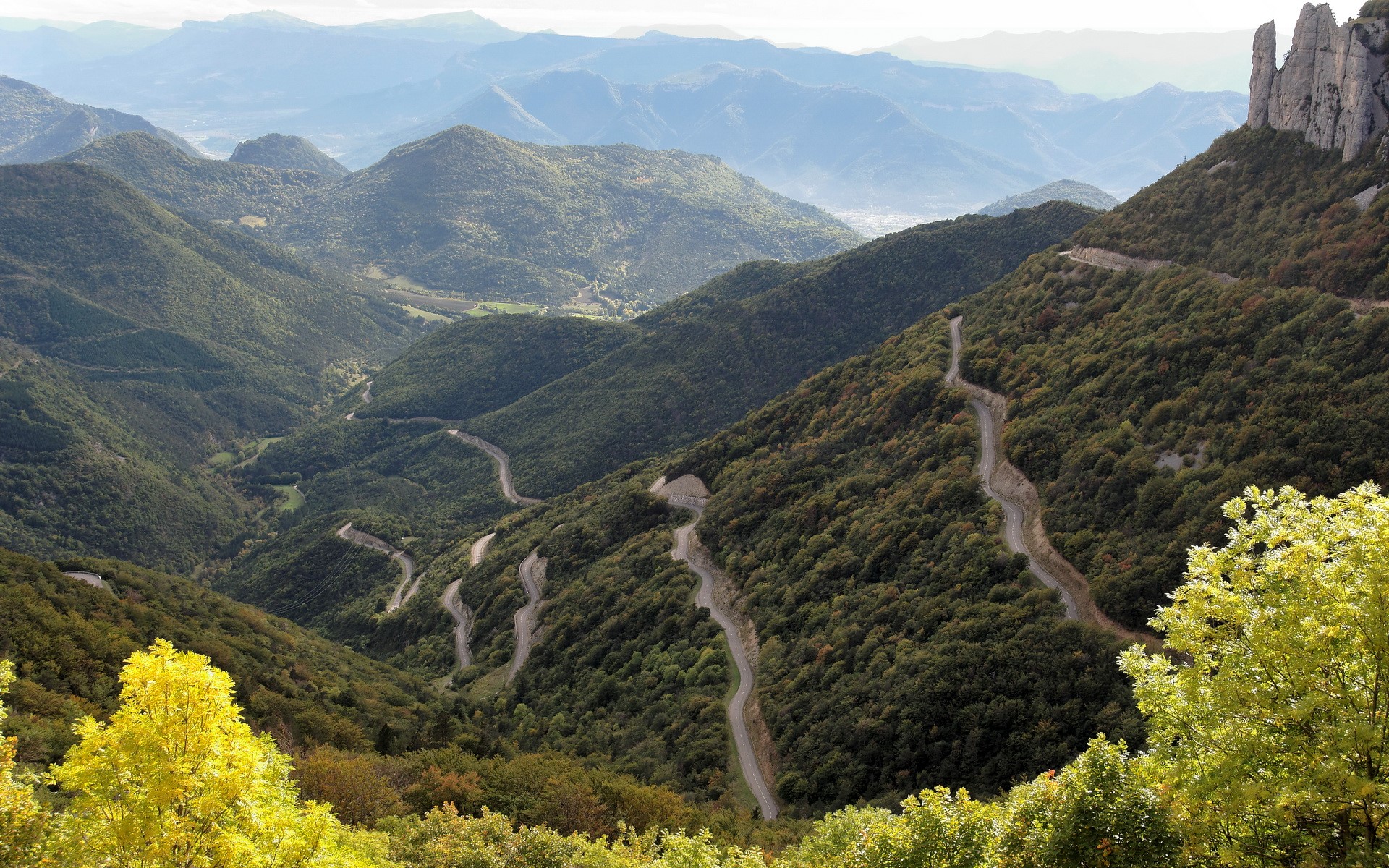 Winding mountain road through forested hills HD Wallpaper