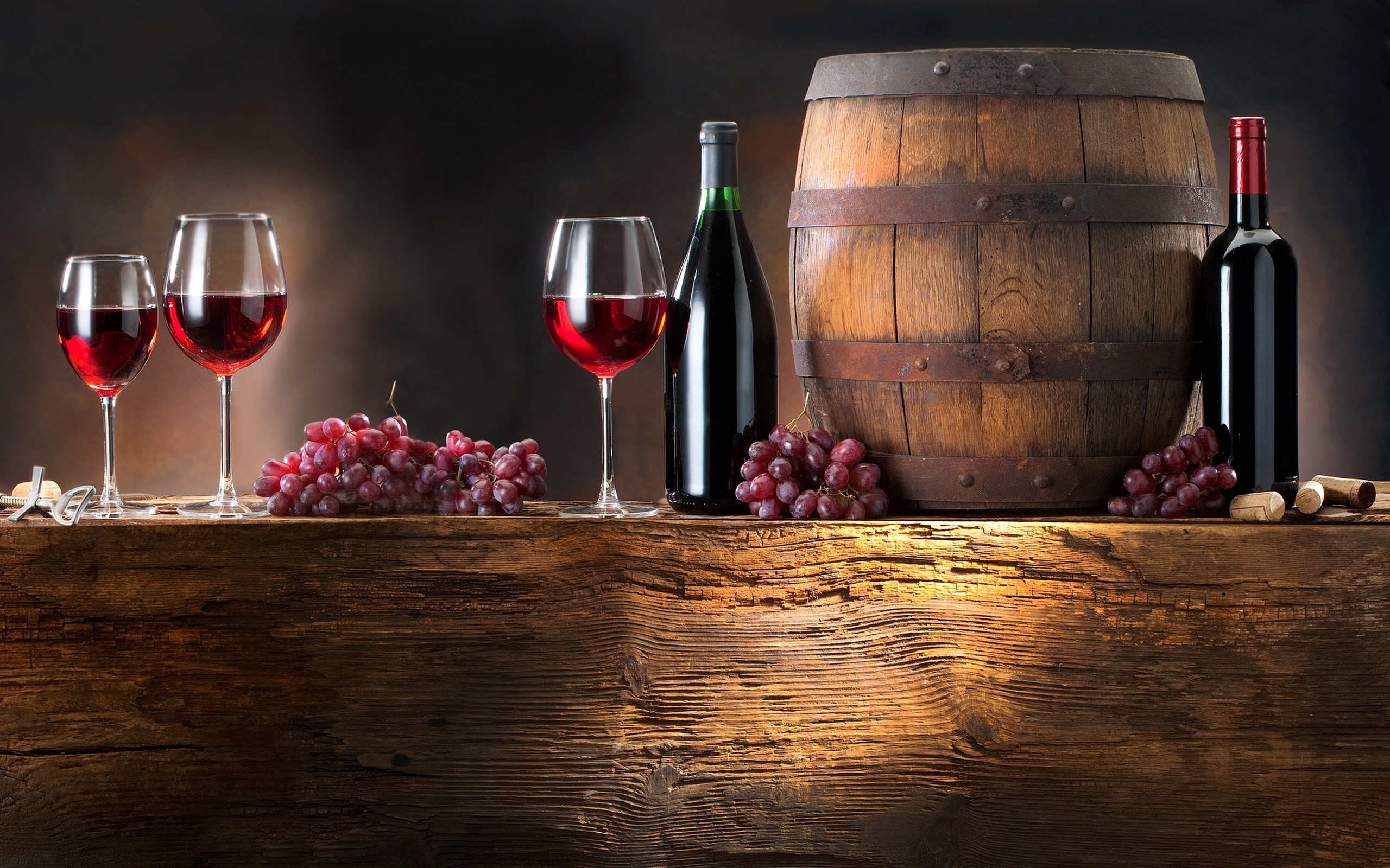 Wine bottles, glasses, grapes, and barrel on a wooden table HD Wallpaper