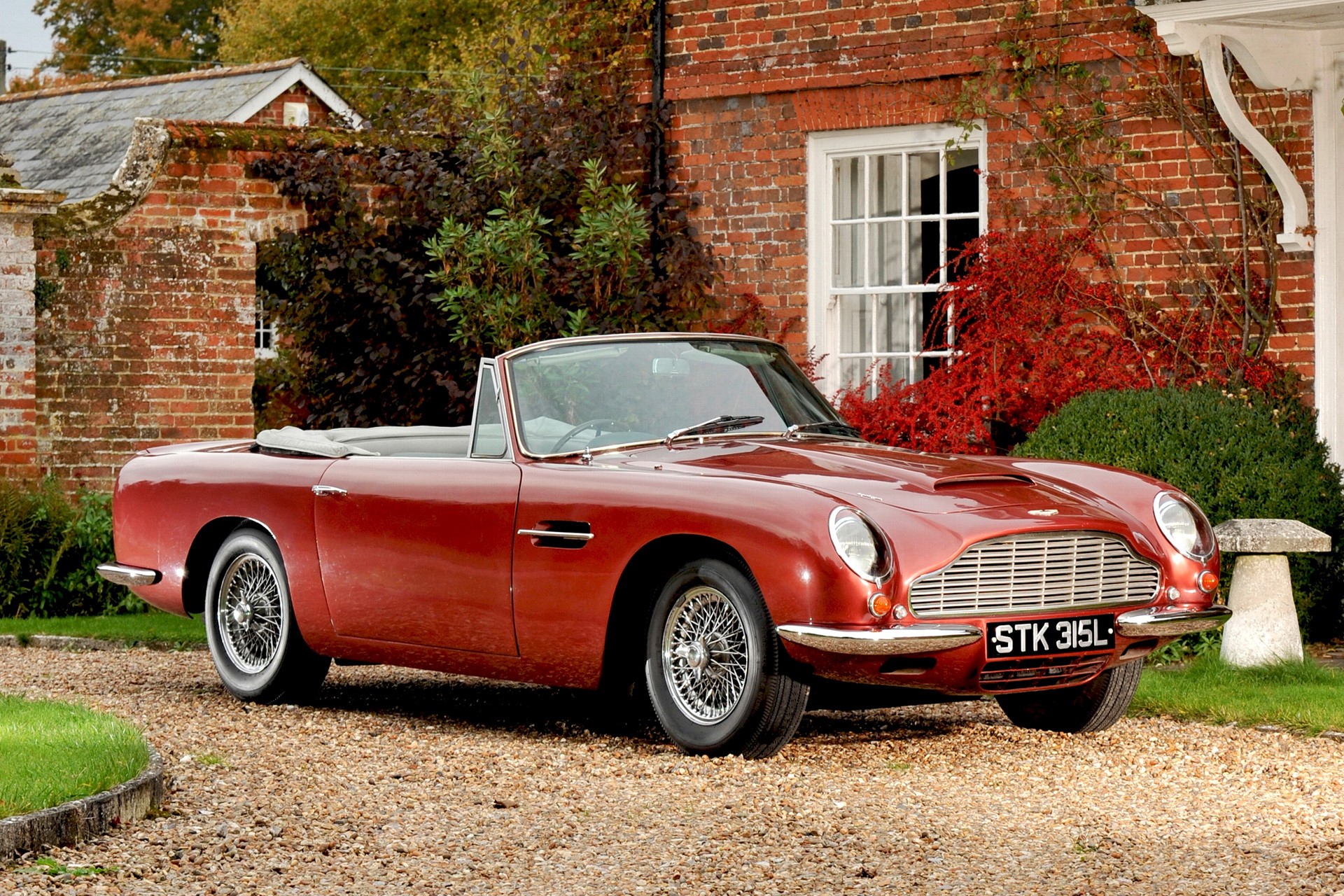 Red Aston Martin DB5 Convertible parked outside brick house HD Wallpaper