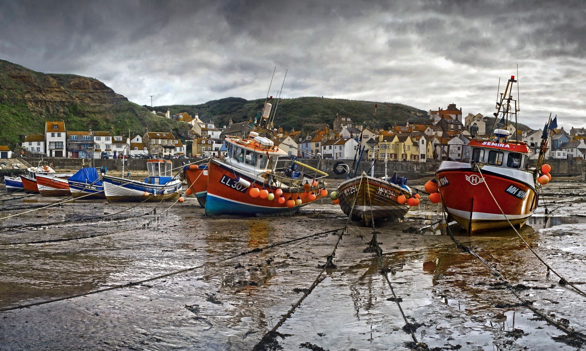 Fishing boats moored on a muddy shore with a town in the background HD Wallpaper
