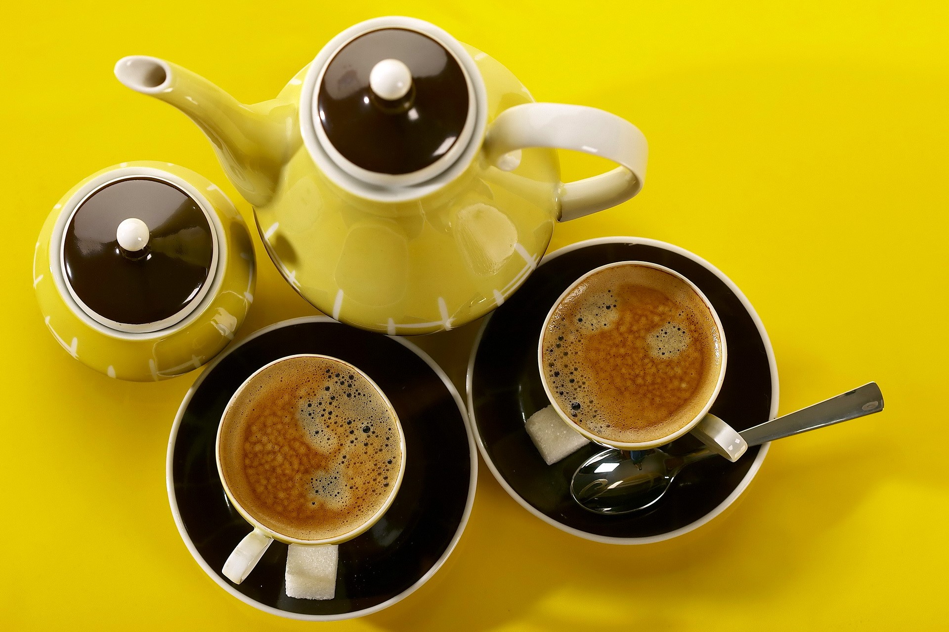Yellow teapot, sugar bowl, and two cups of coffee on yellow background HD Wallpaper