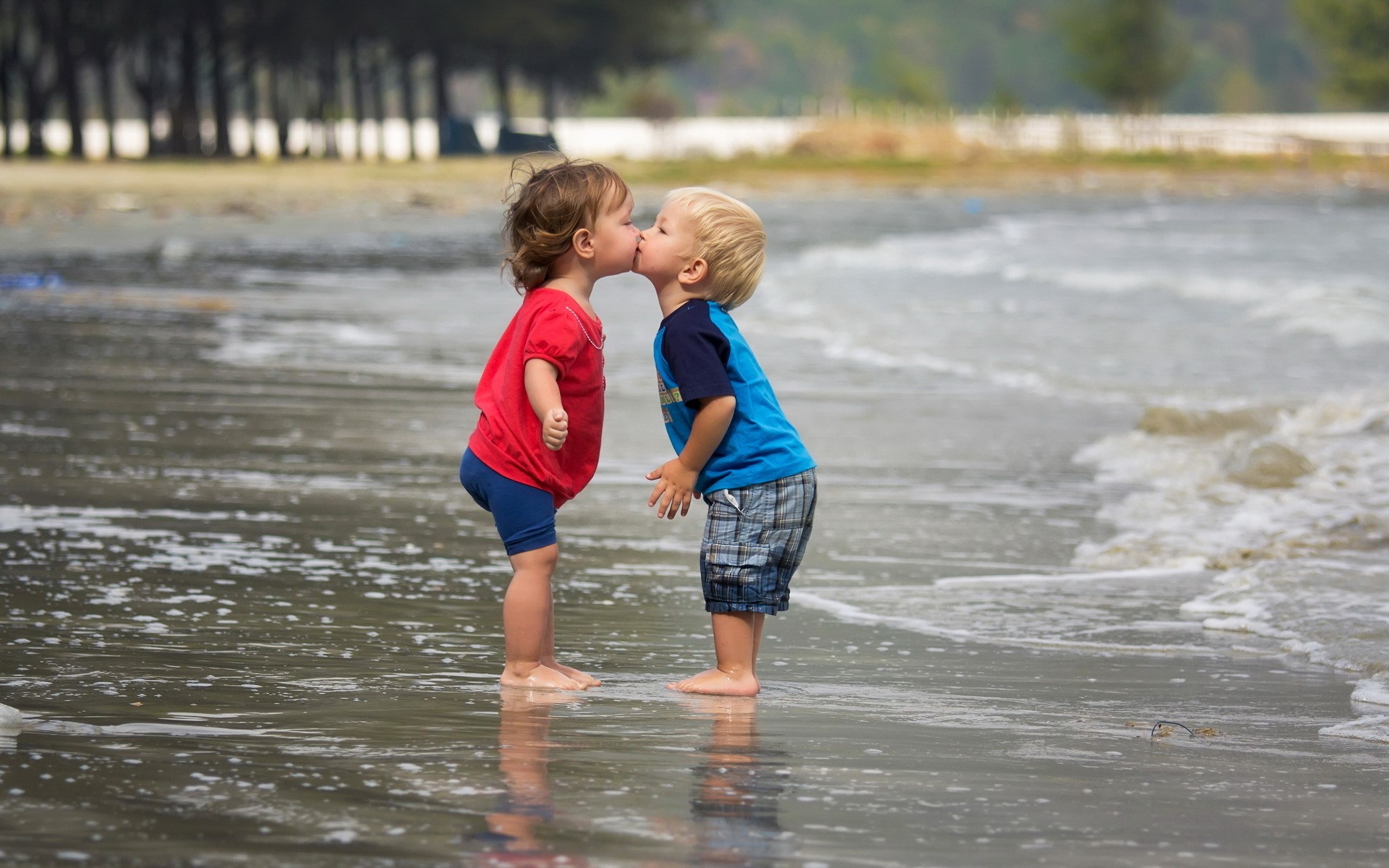 Two young children kissing on a beach HD Wallpaper