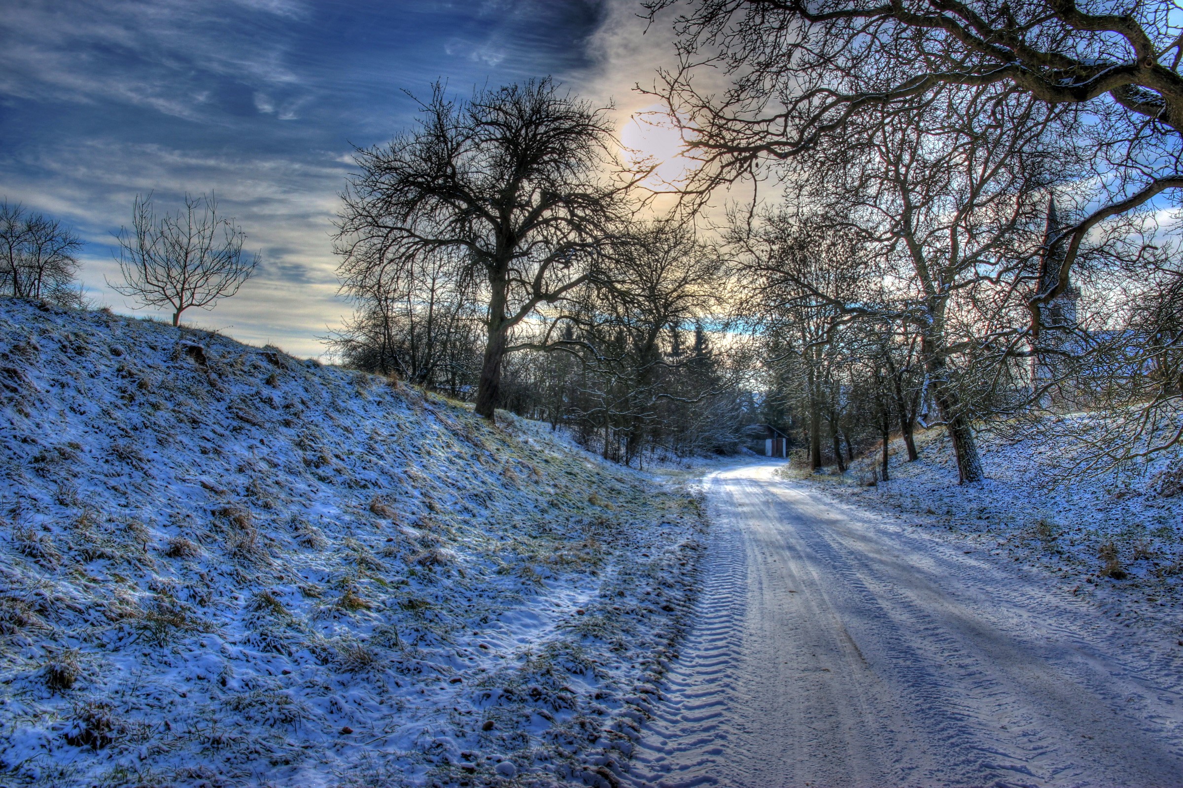 Snowy road through a winter landscape with bare trees HD Wallpaper