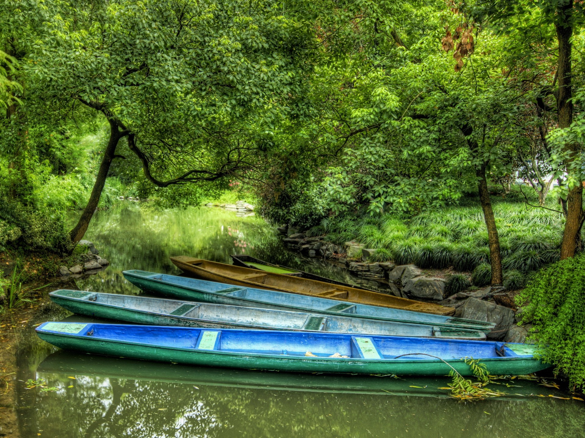 Boats docked on a tranquil canal surrounded by lush greenery HD Wallpaper