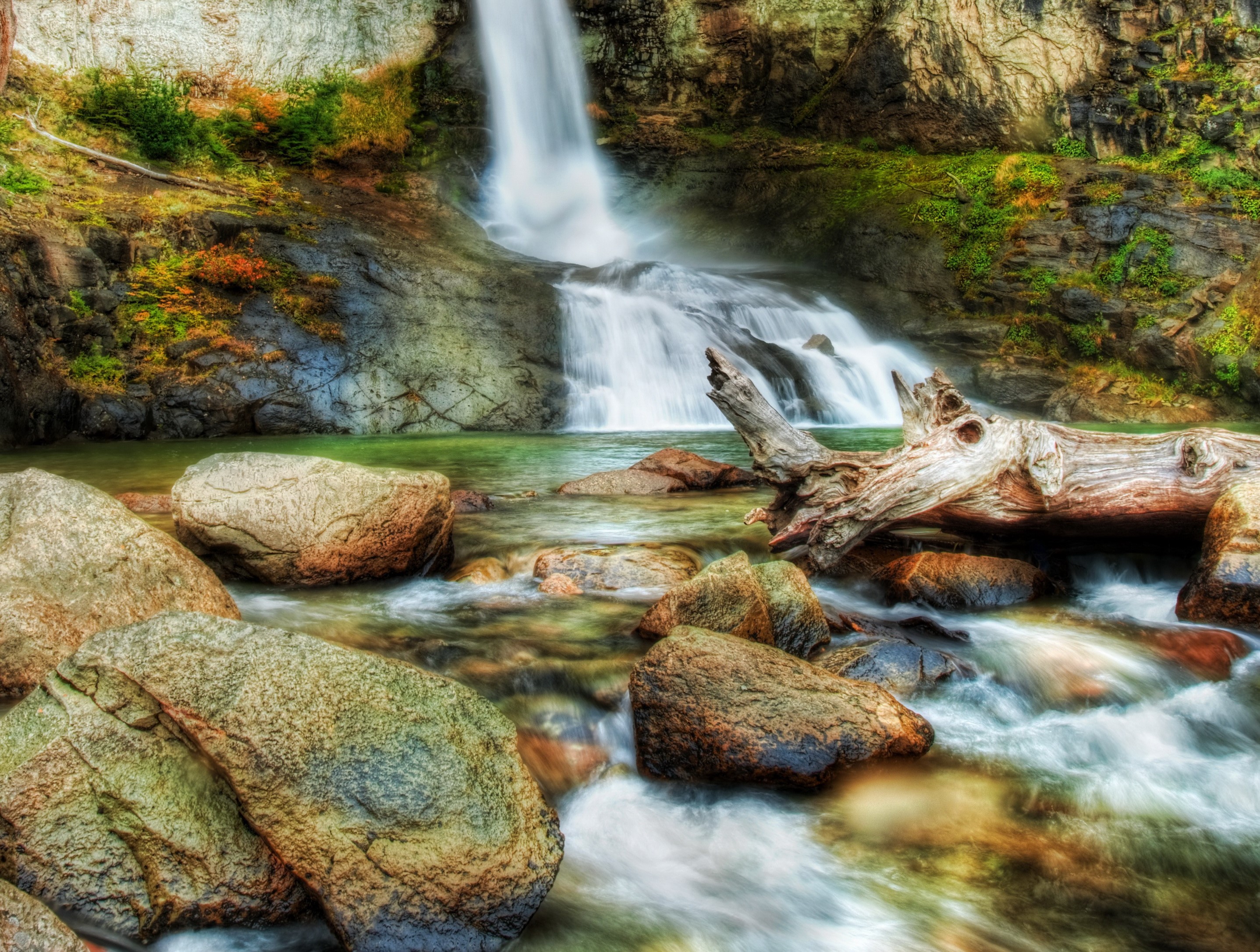 Waterfall cascading over rocks with a fallen log HD Wallpaper
