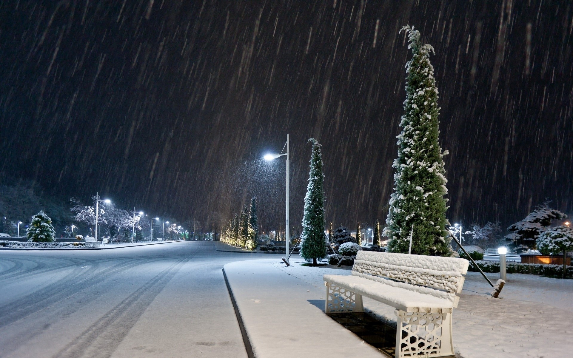 Snowy night in a park with street lights and a bench HD Wallpaper