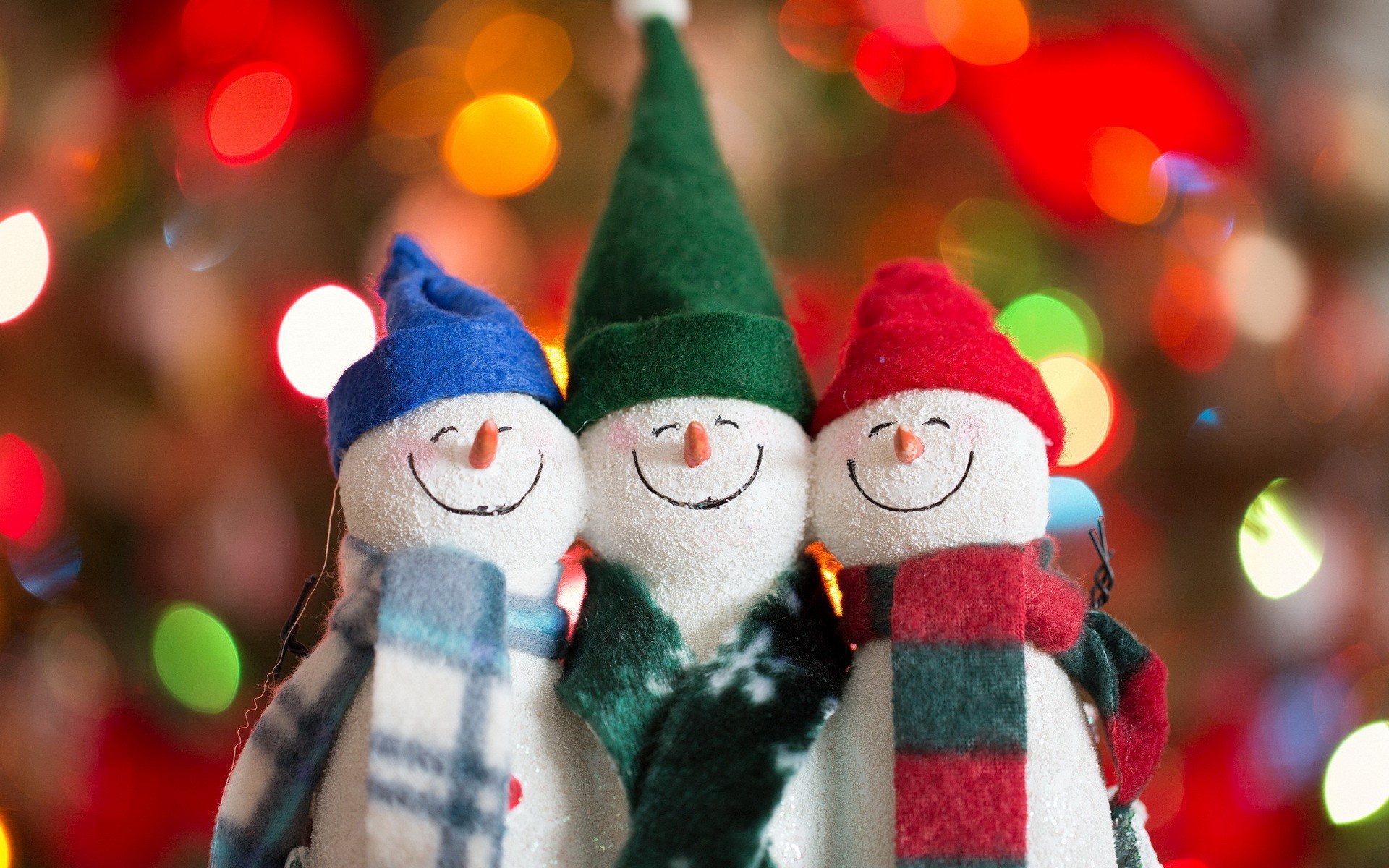 Three snowmen with hats and scarves in front of Christmas lights HD Wallpaper