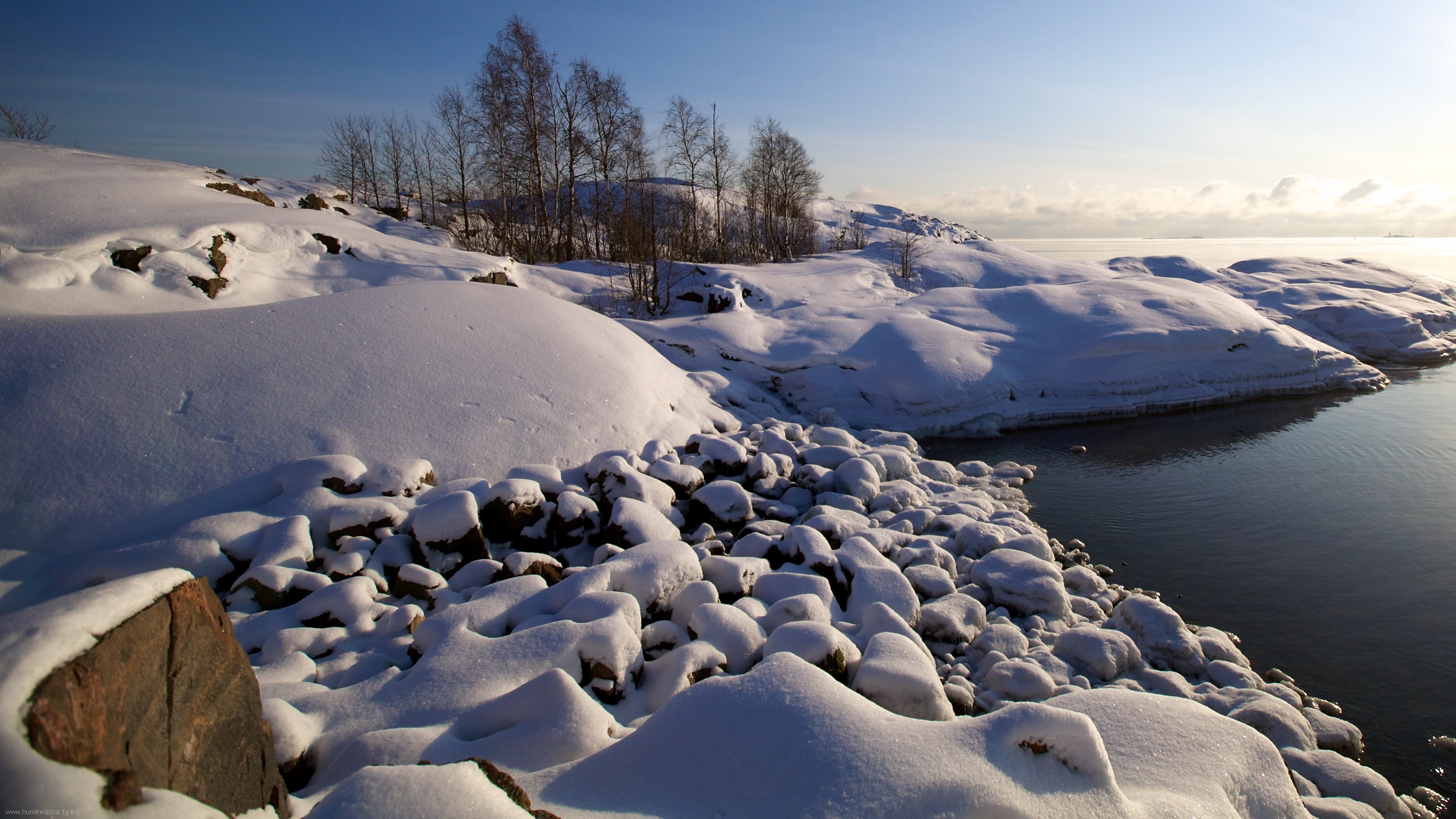 Snowy rocky shore with calm water and trees HD Wallpaper