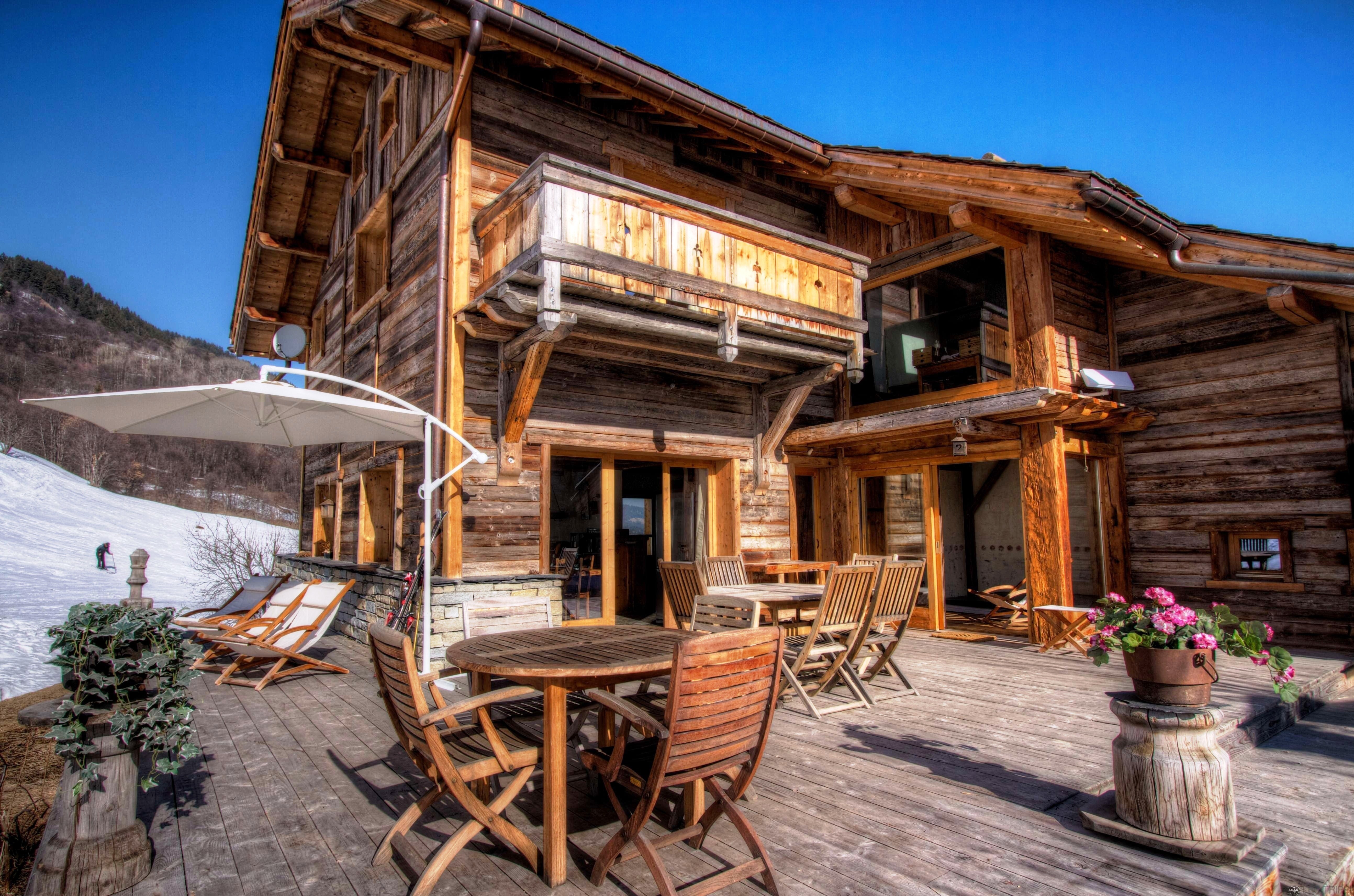 Wooden Chalet with Outdoor Seating and Snowy Mountains HD Wallpaper