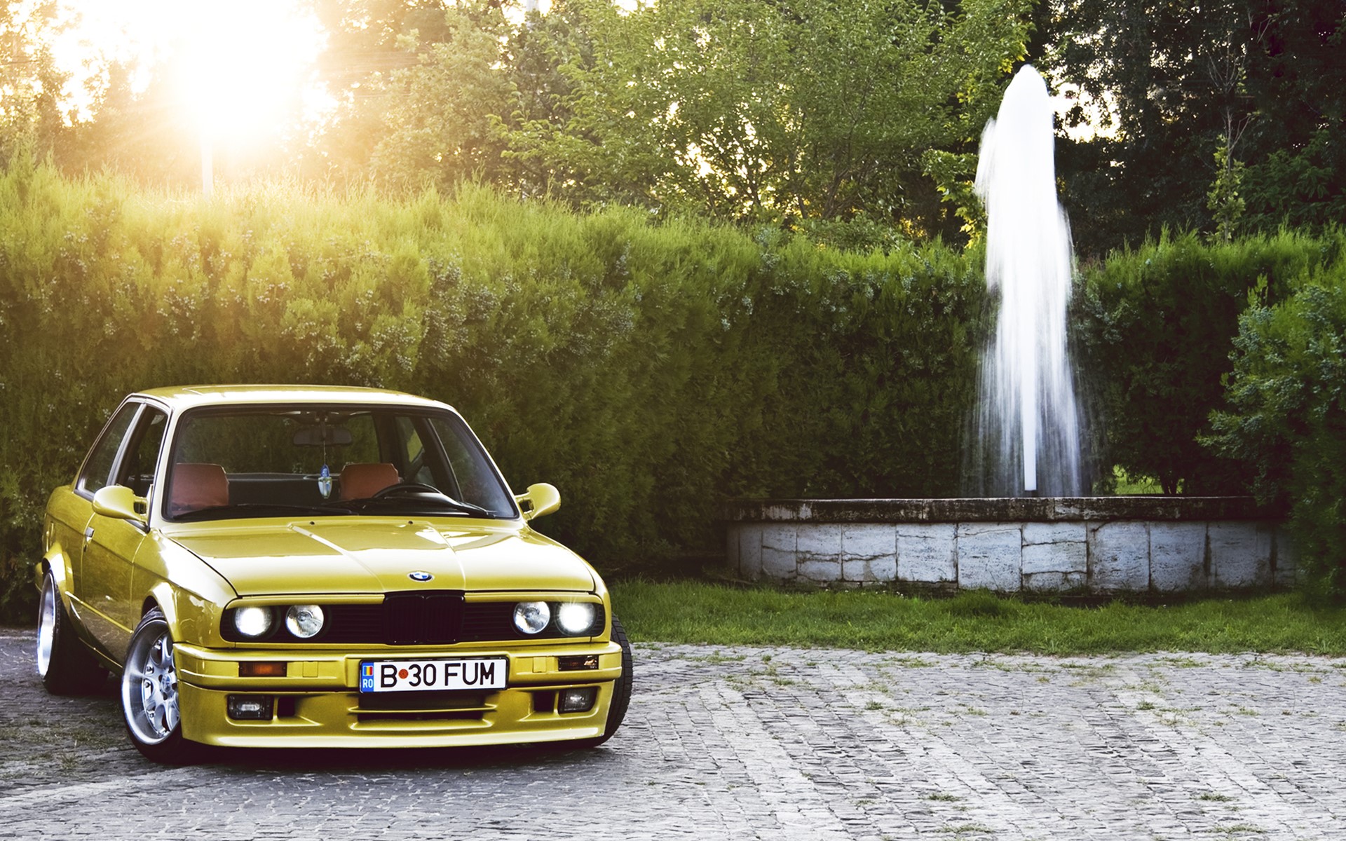 Yellow BMW E30 parked near a fountain HD Wallpaper