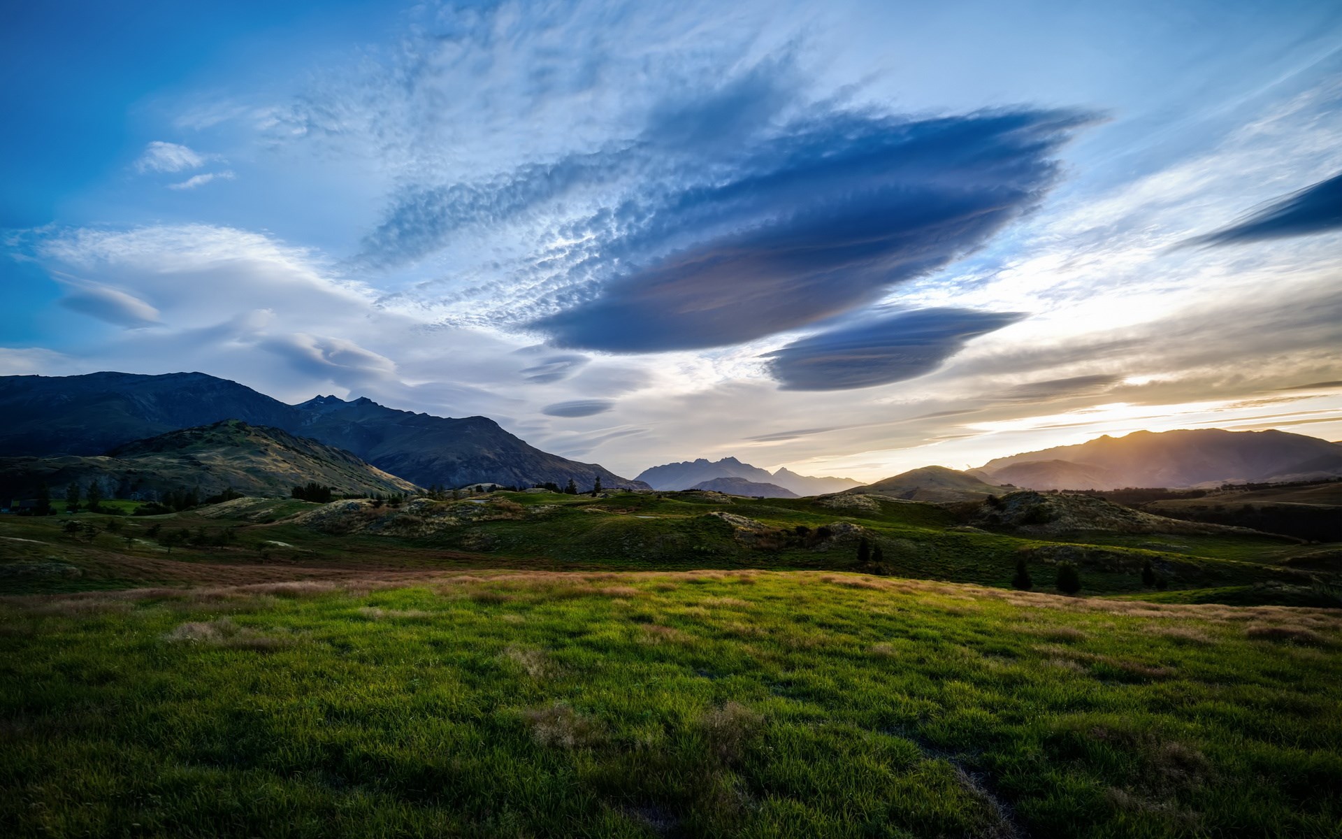 Rolling green hills and mountains under a dramatic sky HD Wallpaper