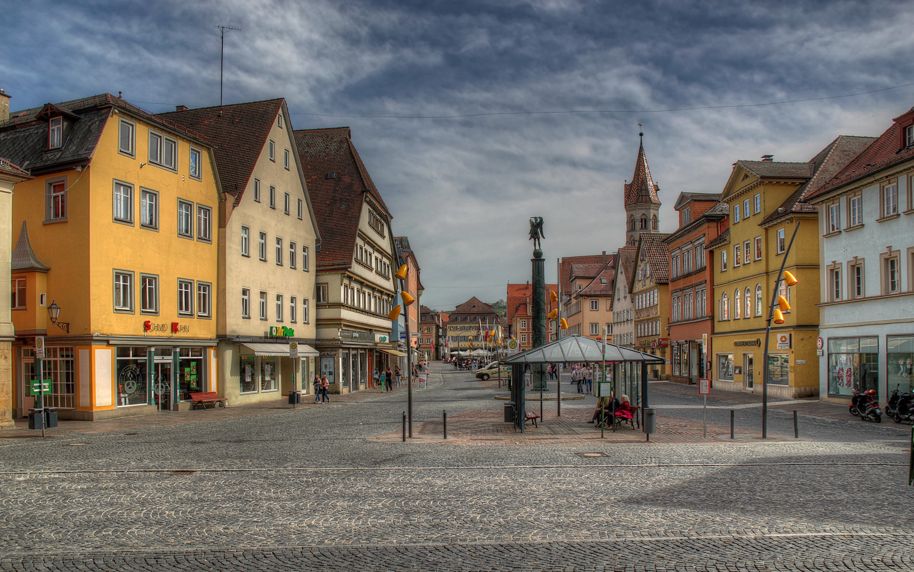 Cobblestone square with colorful buildings and a monument HD Wallpaper