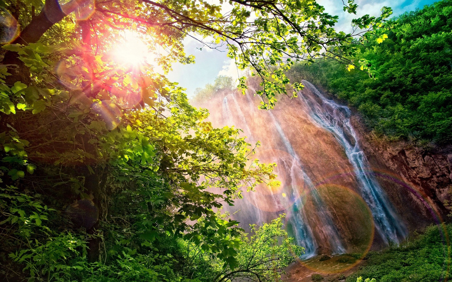 Sunlight filtering through trees onto a waterfall HD Wallpaper